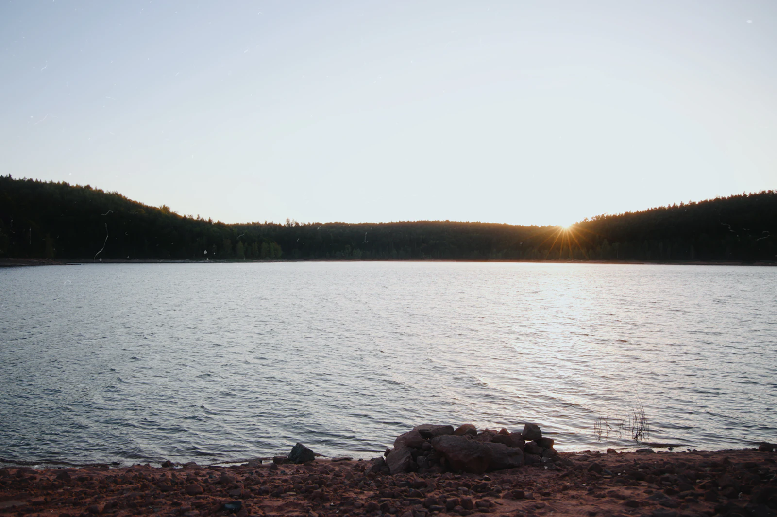 Low sun over a calm lake with a wooded shoreline.