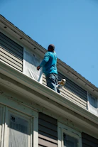 A person in a blue shirt masking a window with plastic film on a house