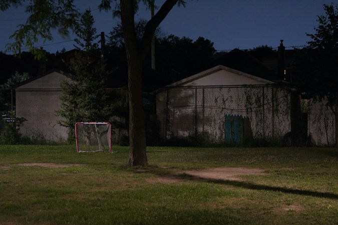 A small street hockey net sitting on a grassy front yard at night near a home garage, the kind of setup kids use for ball hockey at home