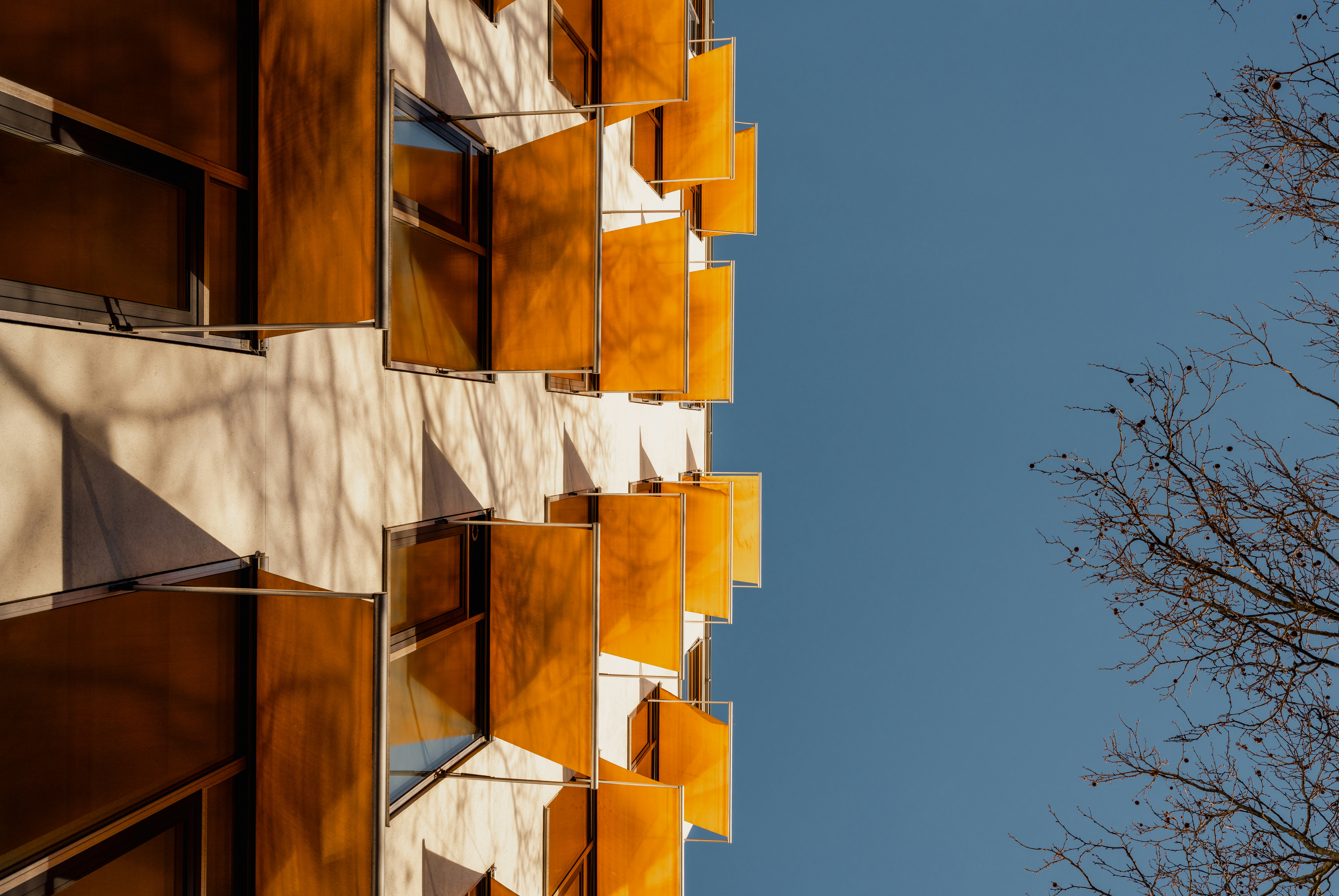 Une façade d’immeuble avec des volets orange ouverts sur un ciel bleu clair