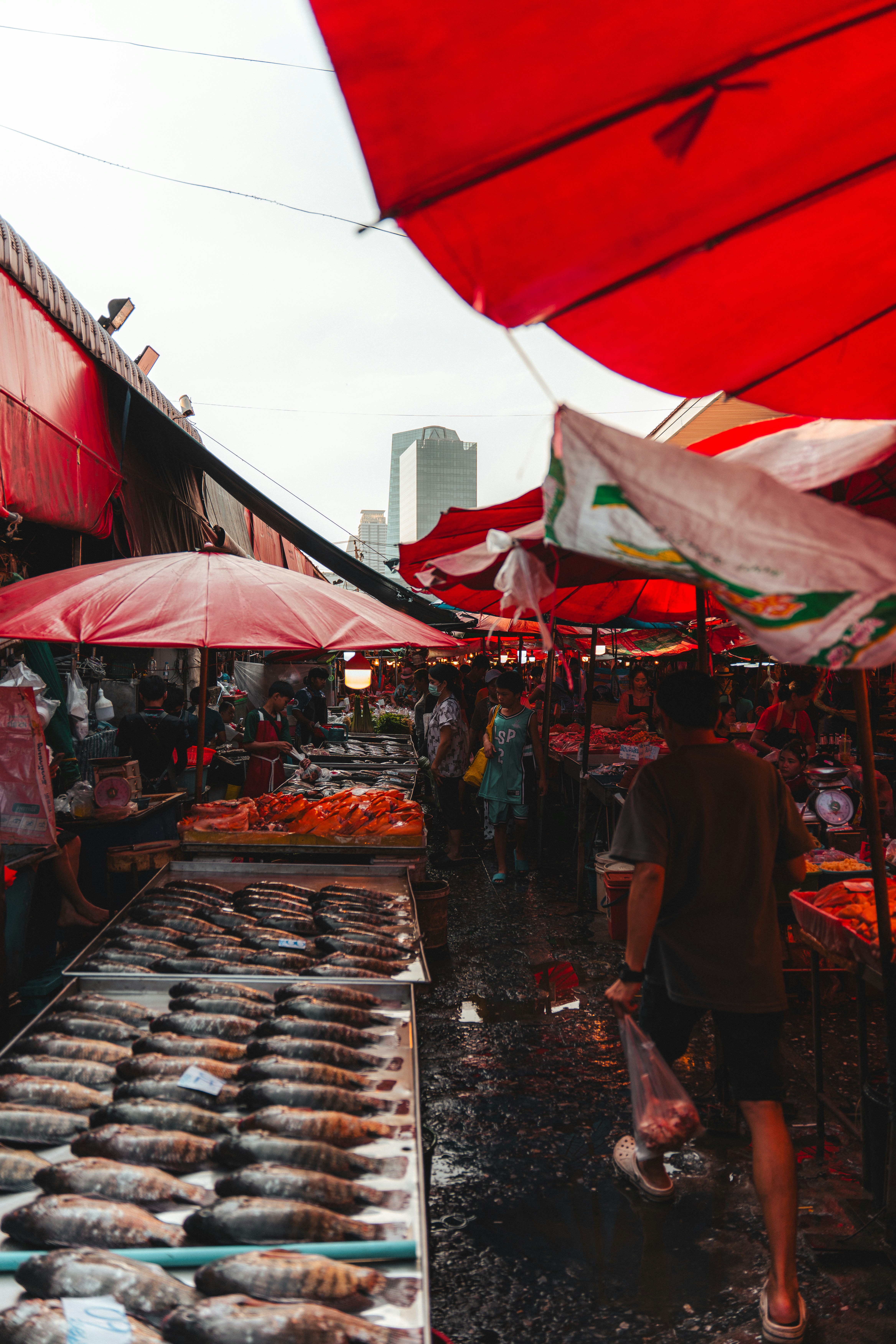 A person walking through a wet outdoor fish market under red umbrellas