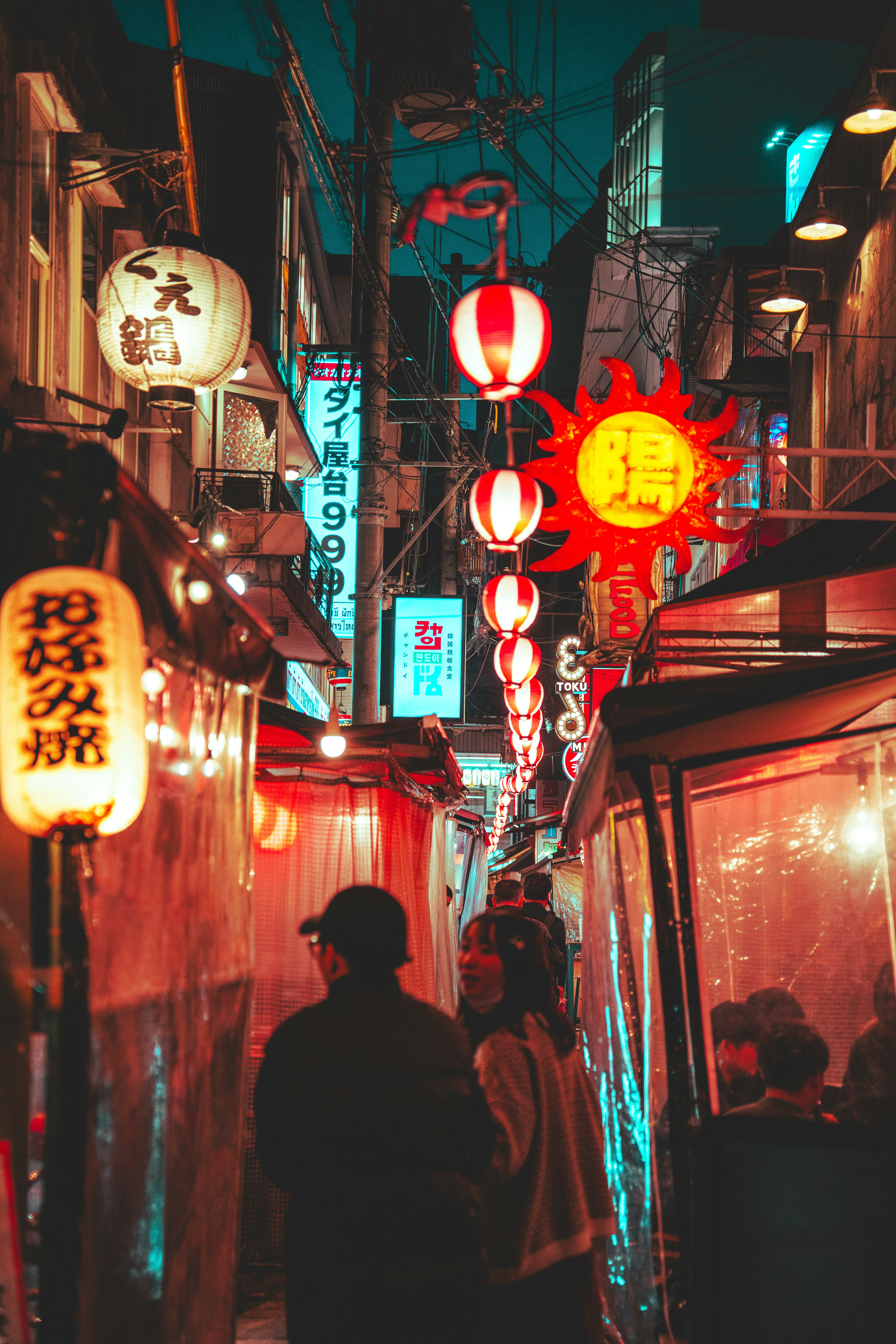 People walking through a narrow street in Japan illuminated by glowing paper lanterns