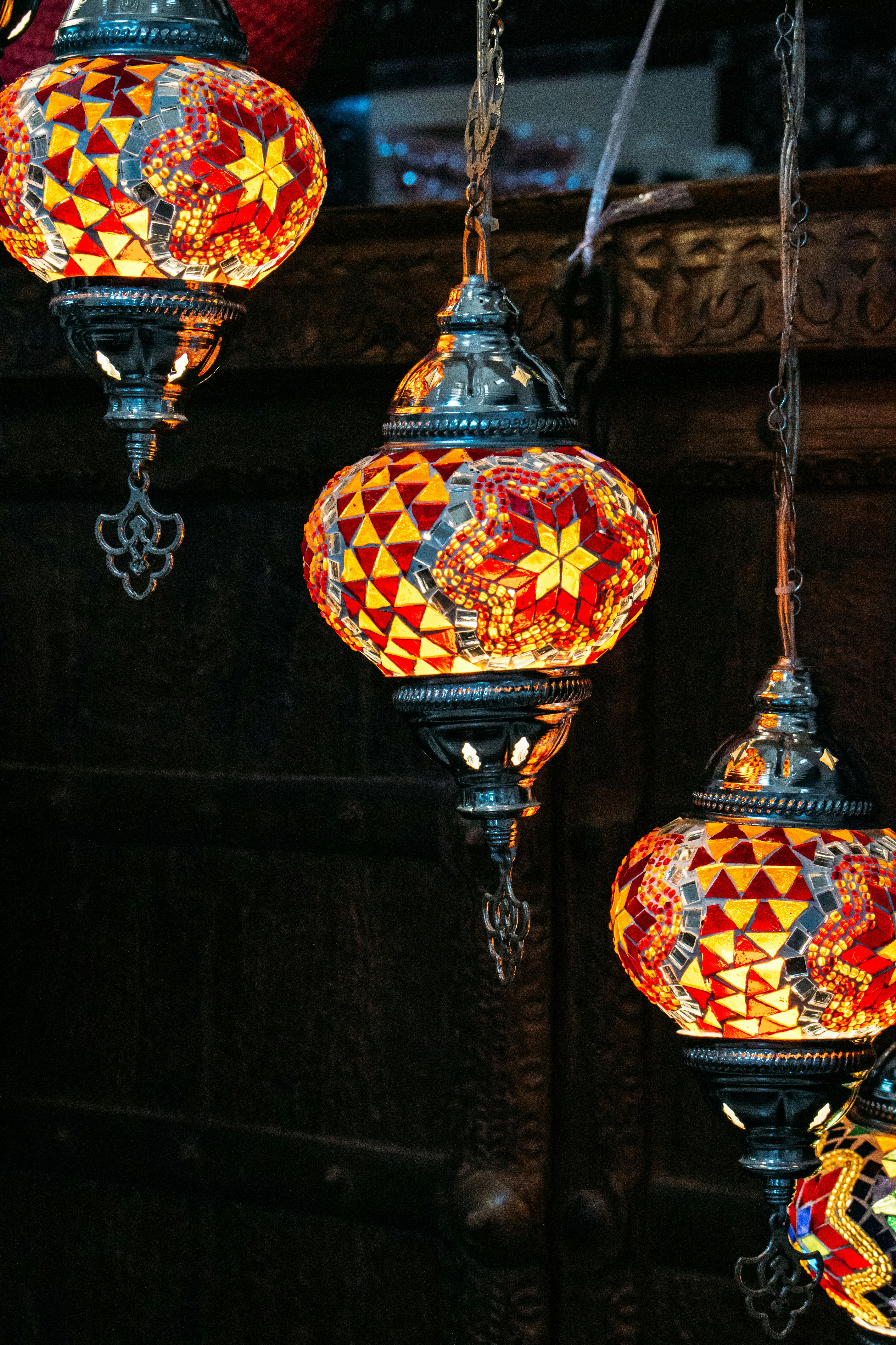 Three colorful mosaic glass lamps hanging against a dark carved wooden background.