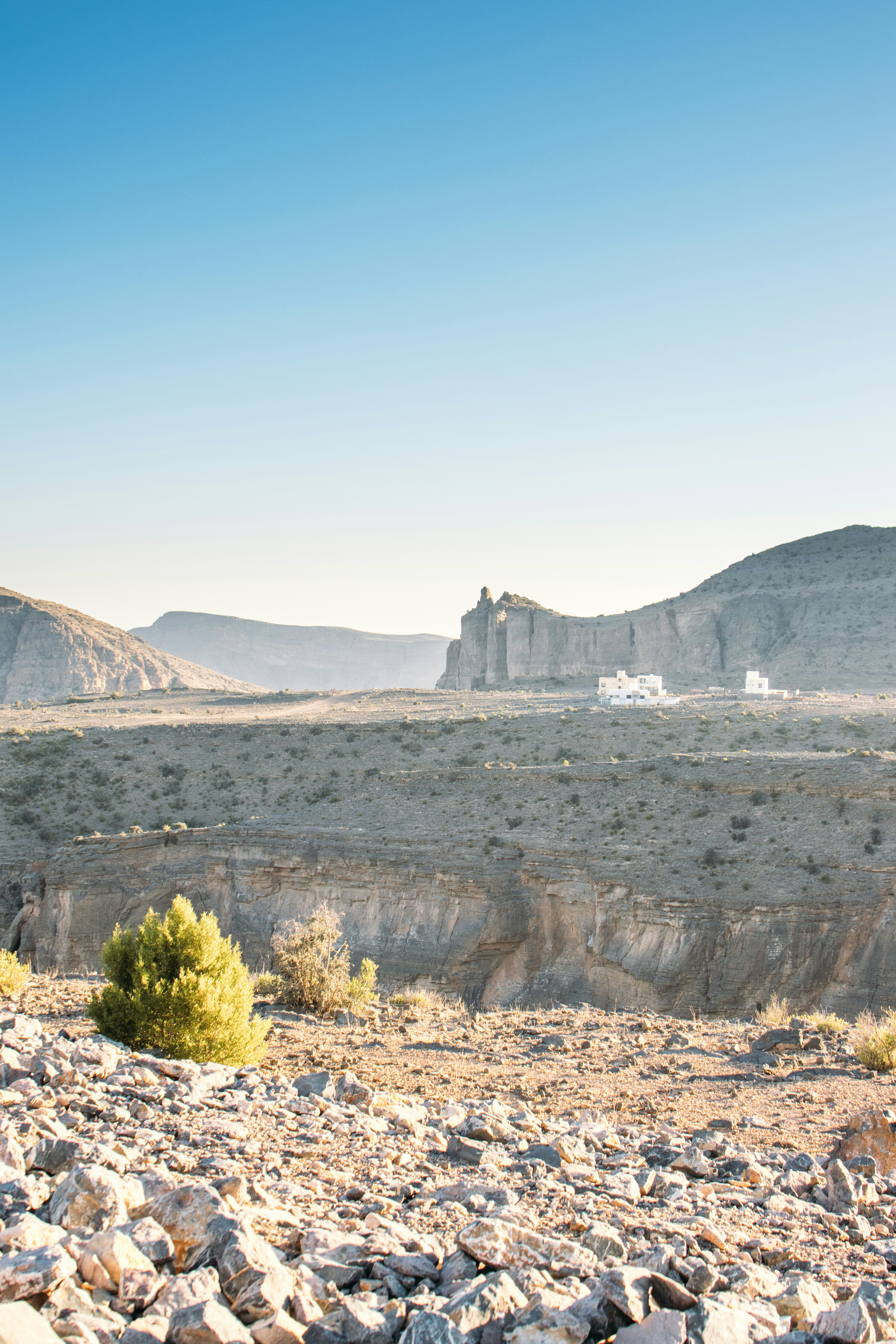 A rocky desert landscape with distant white buildings under a clear blue sky.