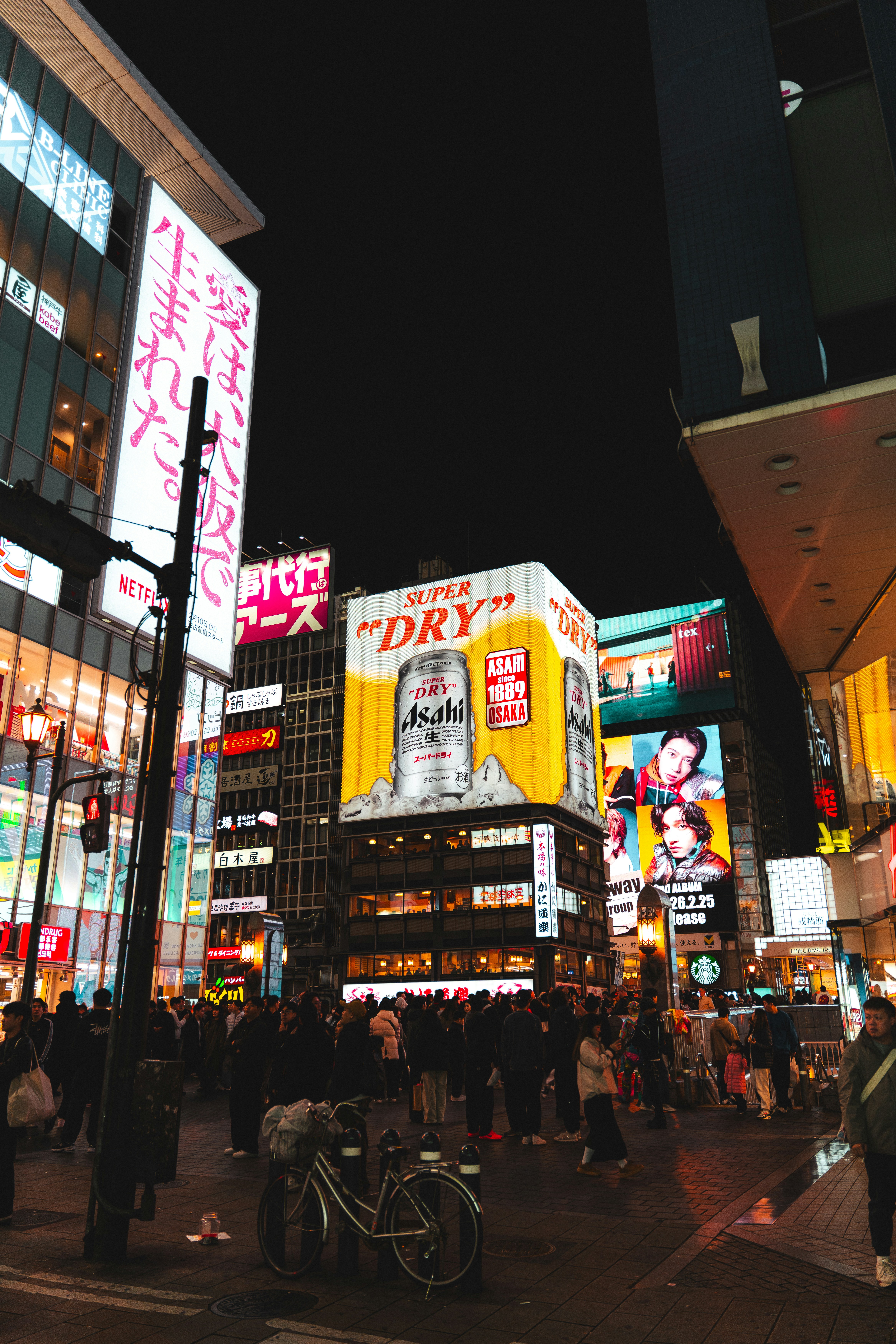 A crowd of people walking through a neon-lit street intersection in Osaka at night.