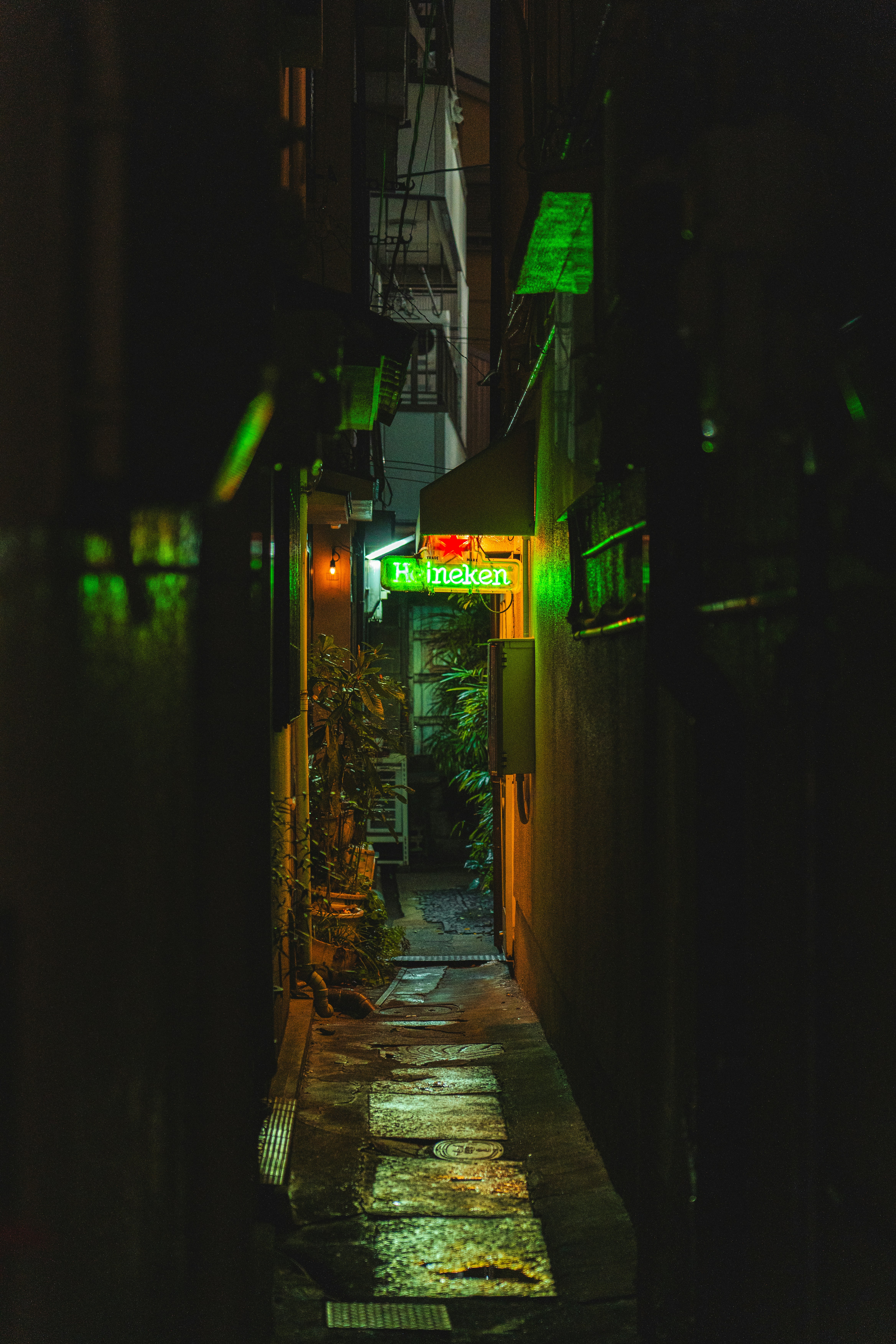 A narrow alleyway at night illuminated by a glowing green neon sign.
