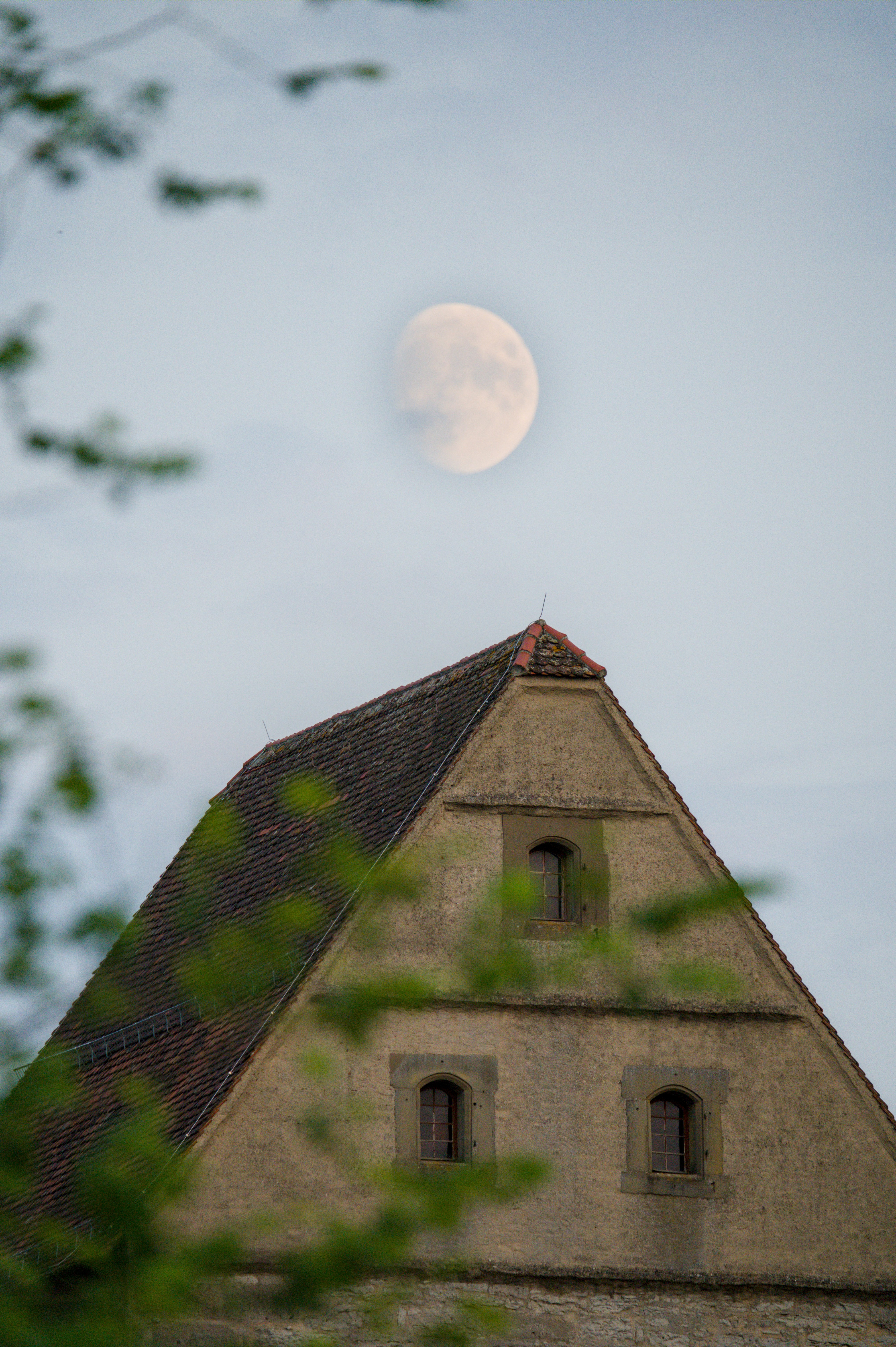 The moon above the gabled roof of an old stone building