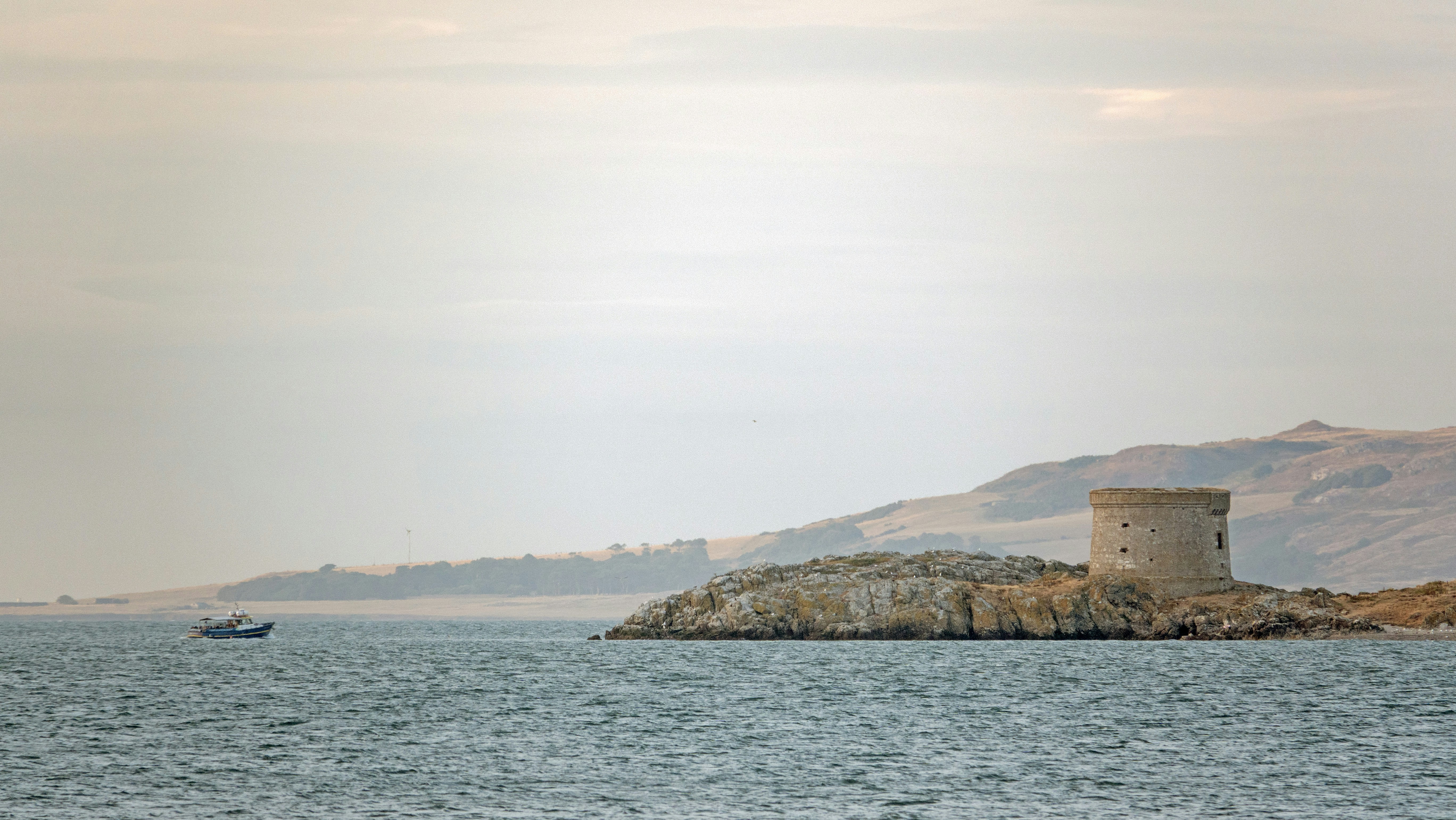 A stone Martello tower on a rocky island with a boat nearby.