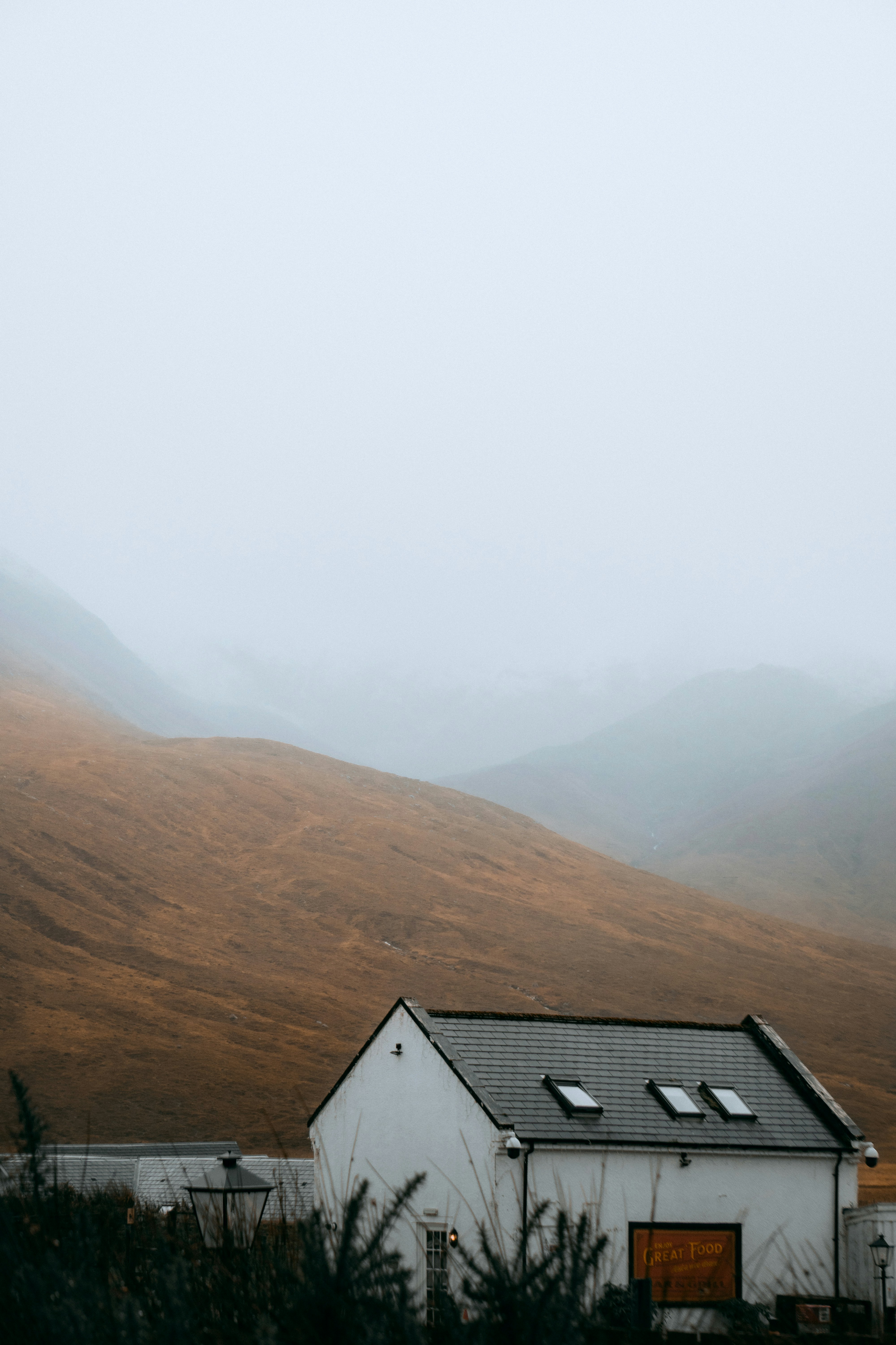 A white building with a dark roof beneath misty brown mountain slopes