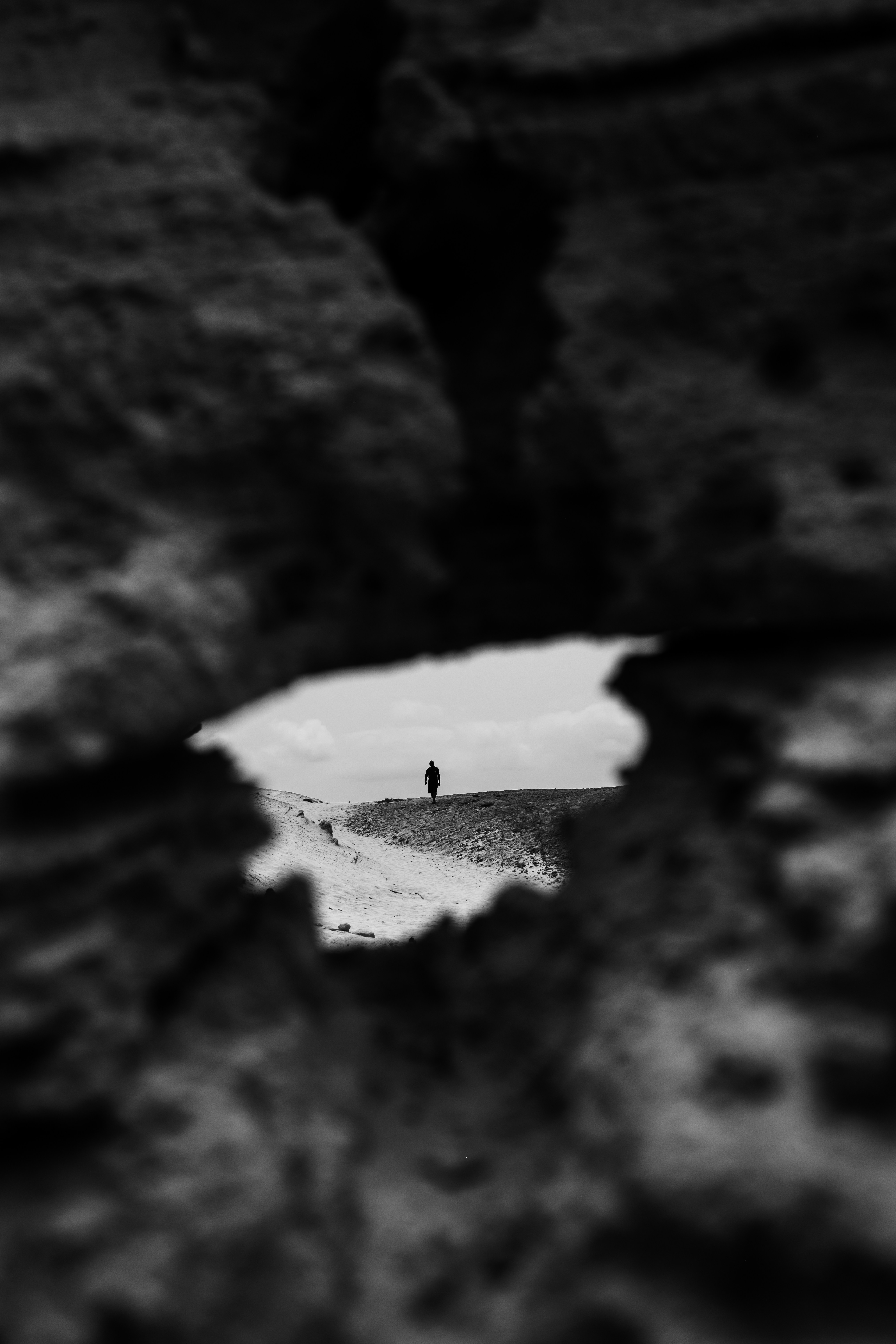 A person in silhouette on a sandy ridge viewed through a rocky opening.