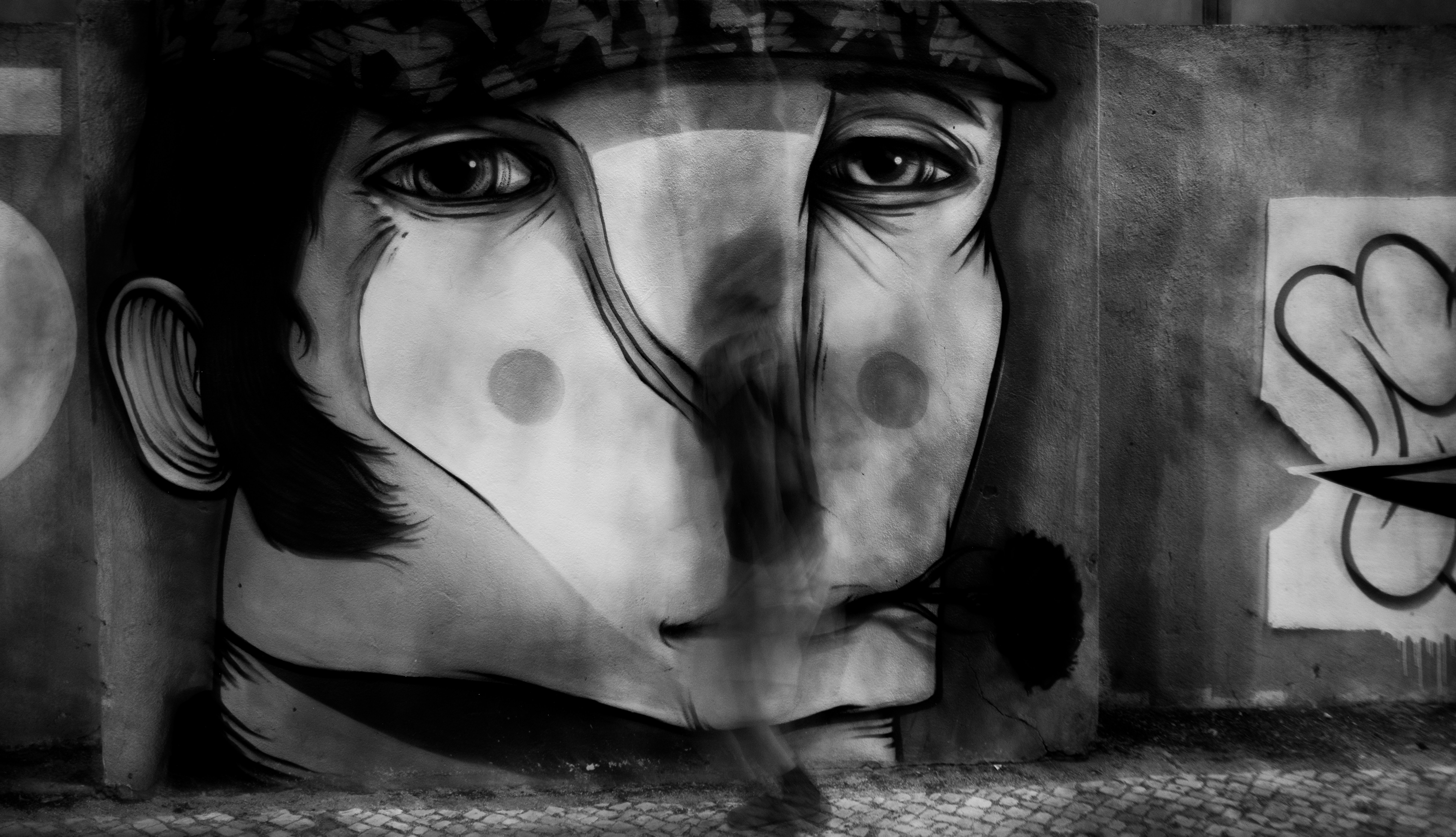 A blurred person walking past a large black and white mural of a face.
