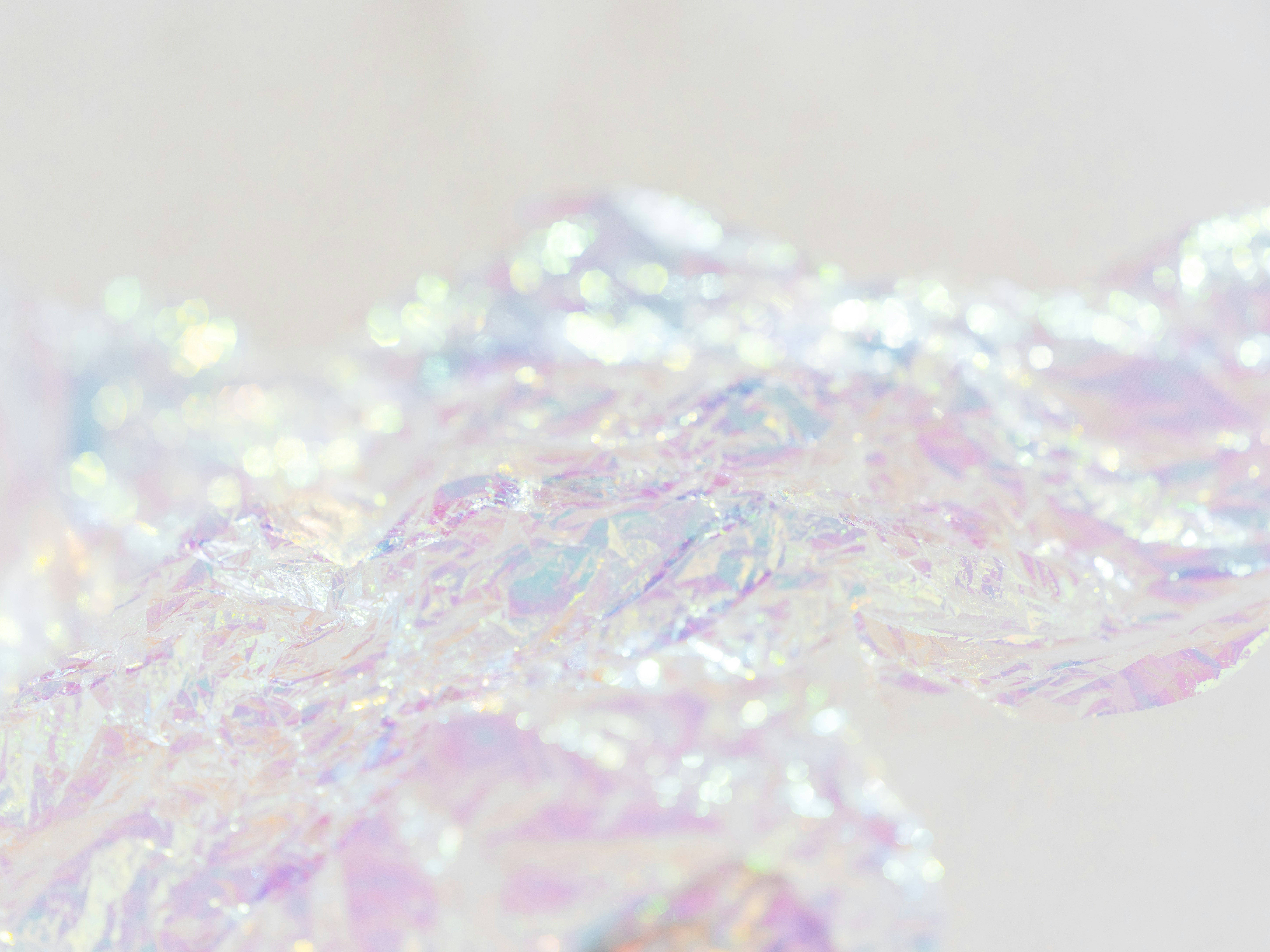 Crumpled iridescent wrapping paper with soft bokeh highlights on a light fabric surface.