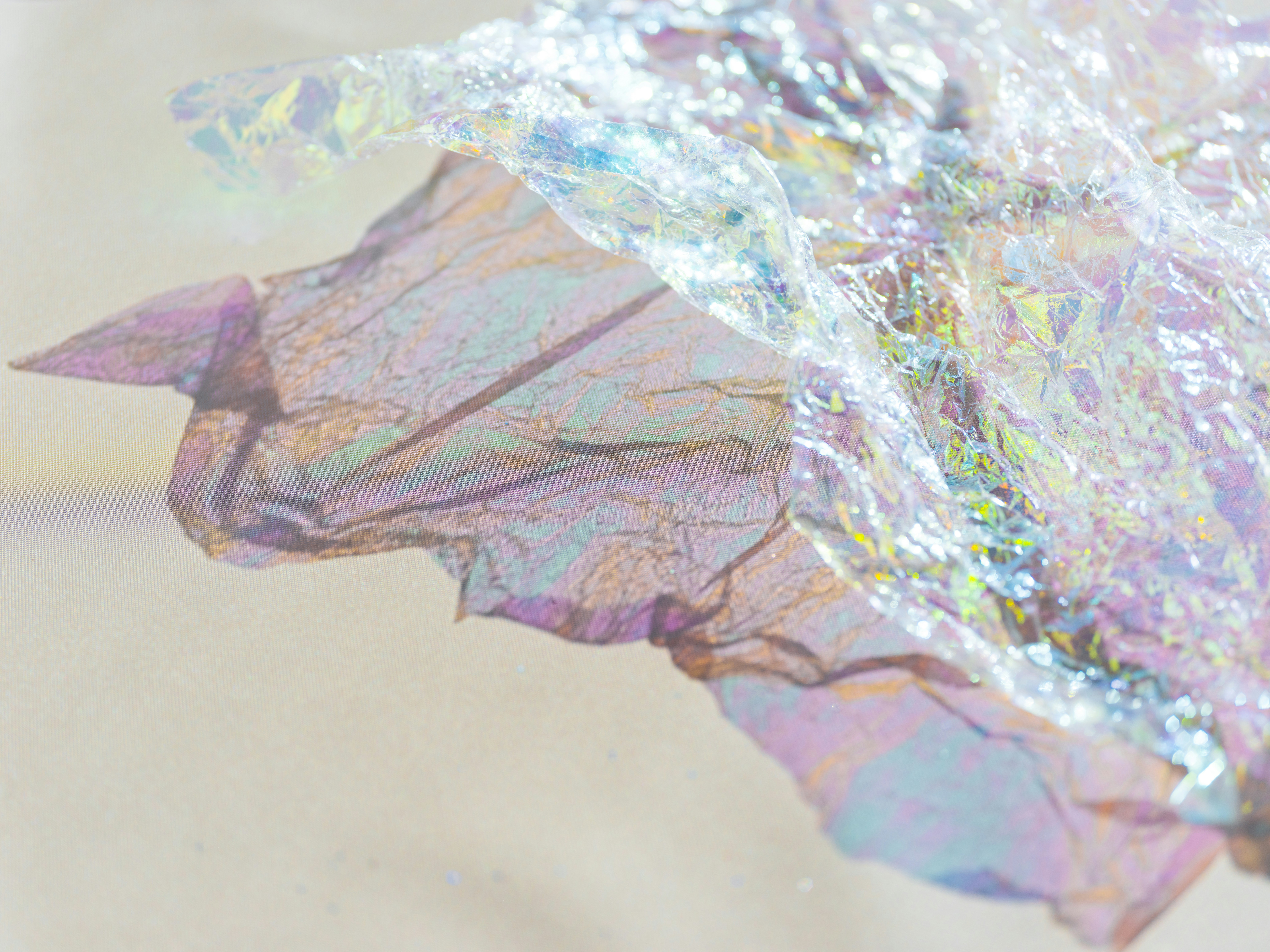 Crumpled iridescent wrapping paper on a beige cloth background with soft shadows.