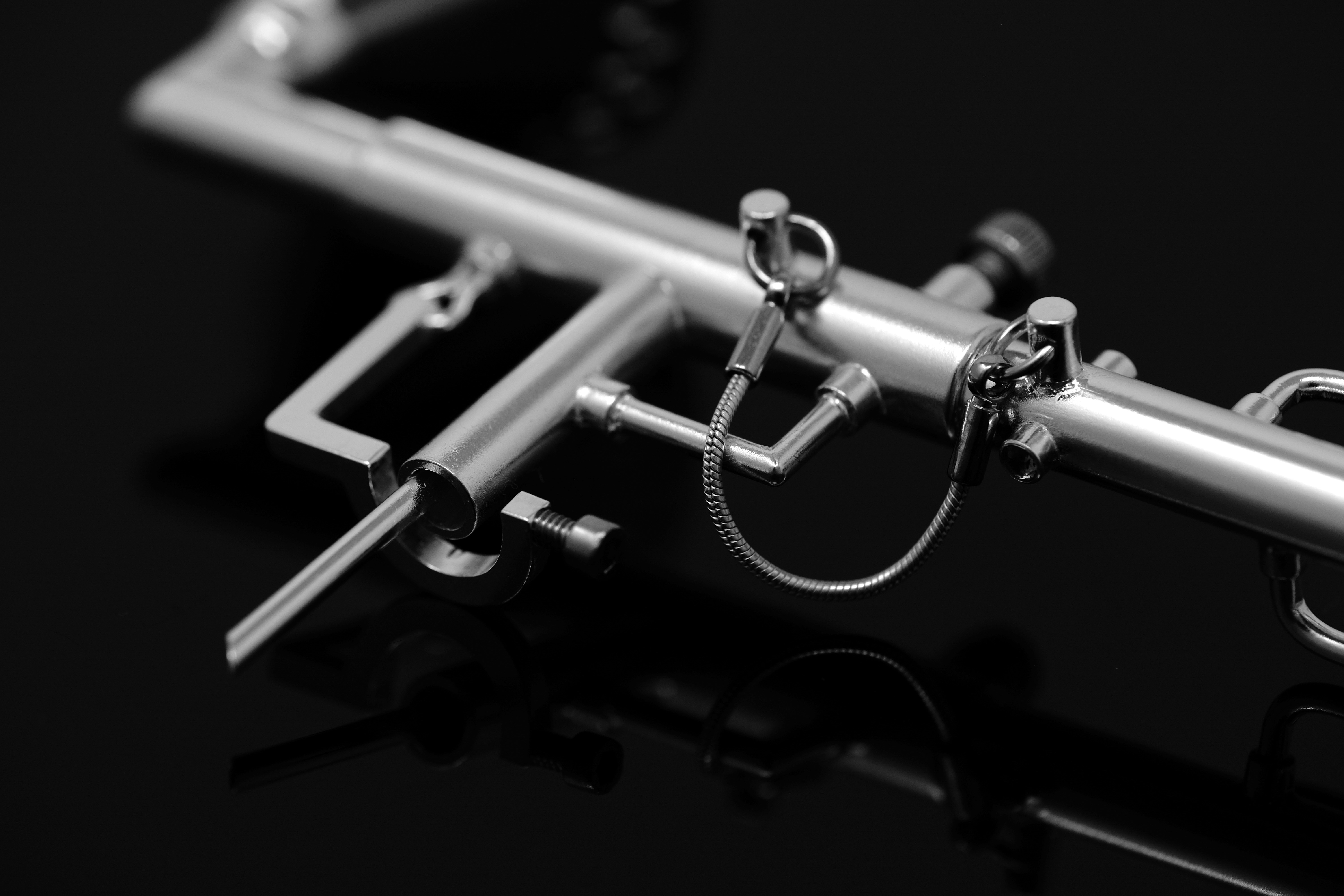 A metallic surgical instrument with a small chain on a black reflective surface