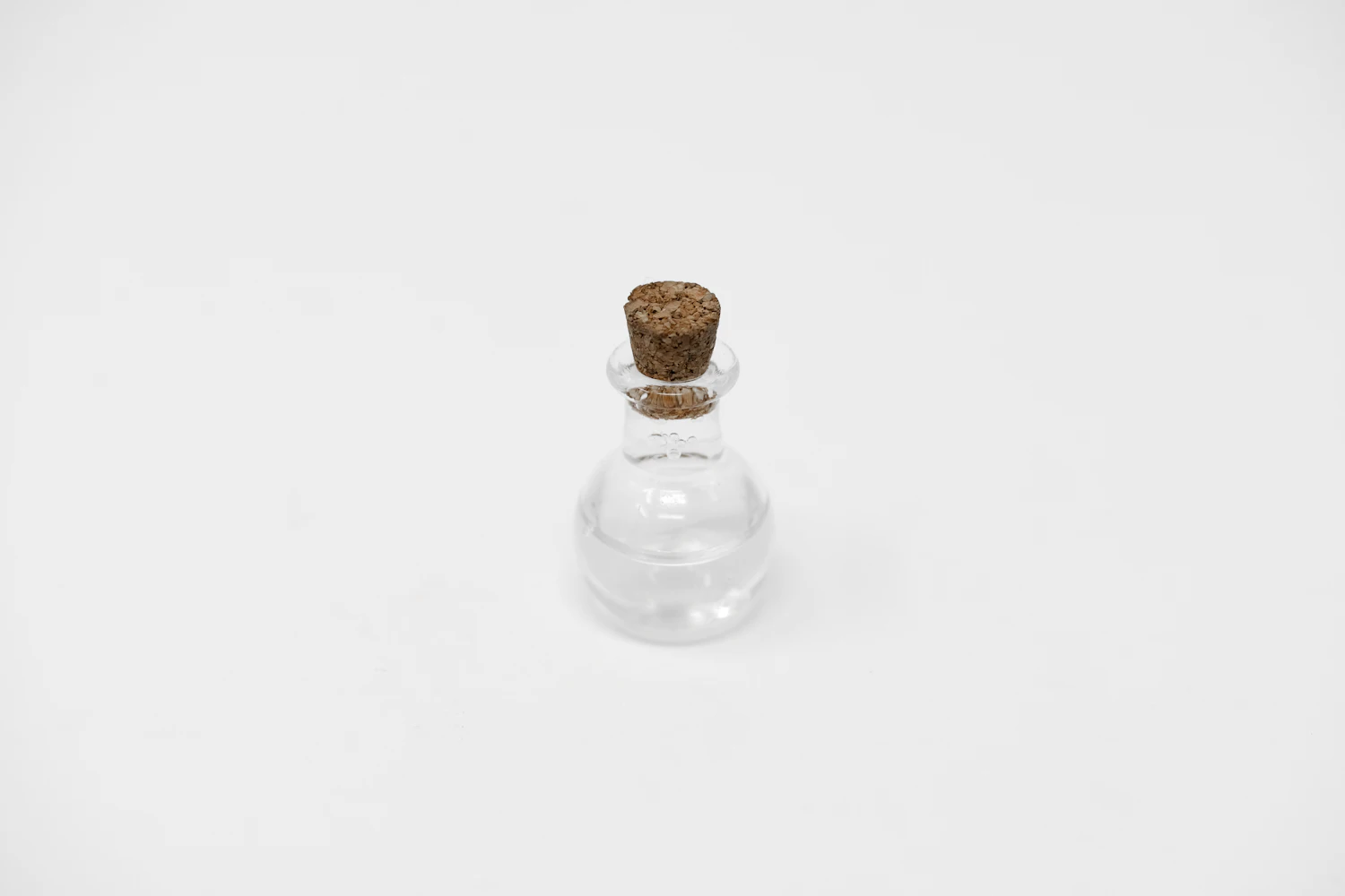 A small round glass bottle with a cork stopper on white
