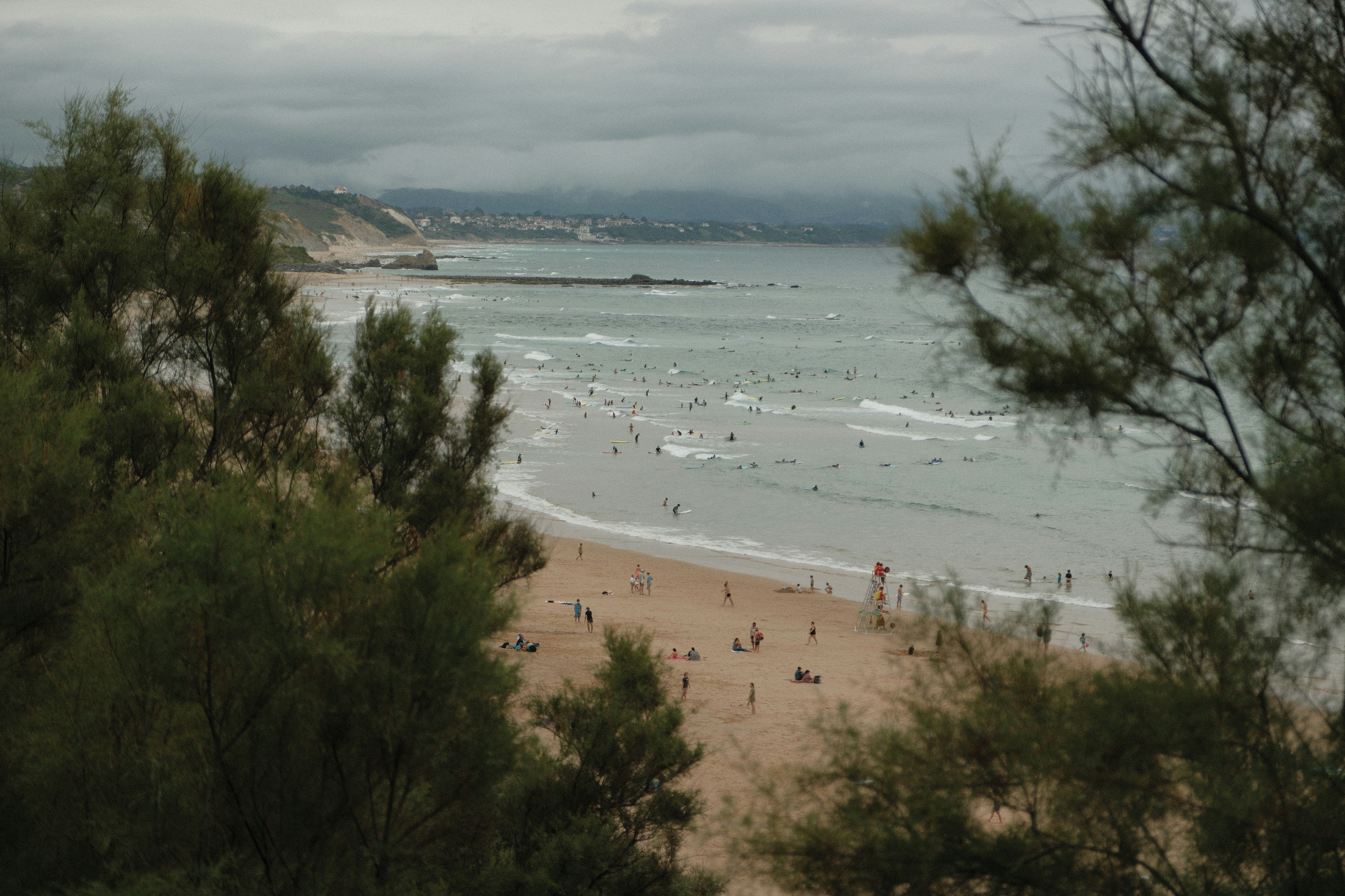 People surfing and relaxing on a sandy beach under a cloudy sky