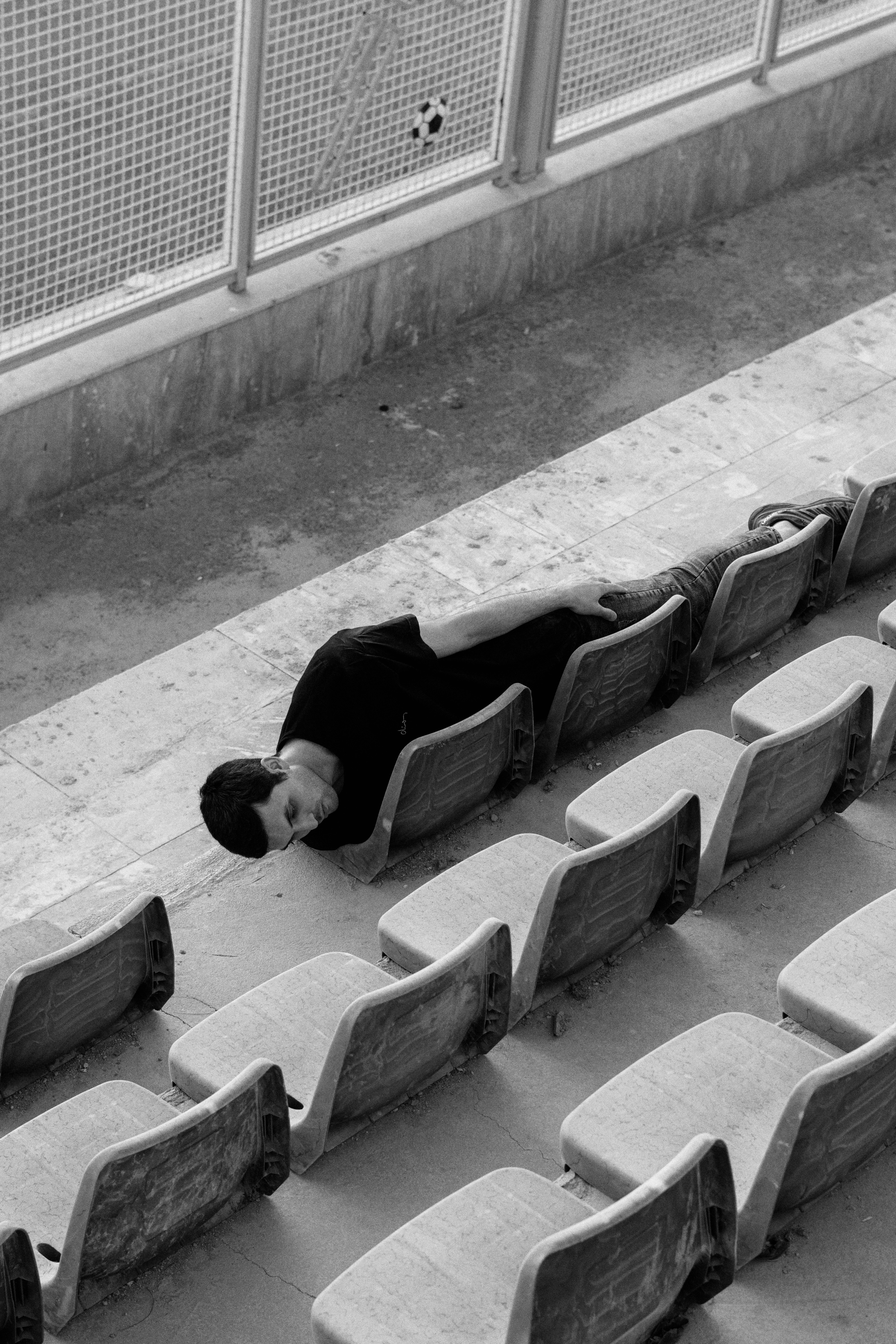 A person in a black t-shirt lying across stadium seats in black and white