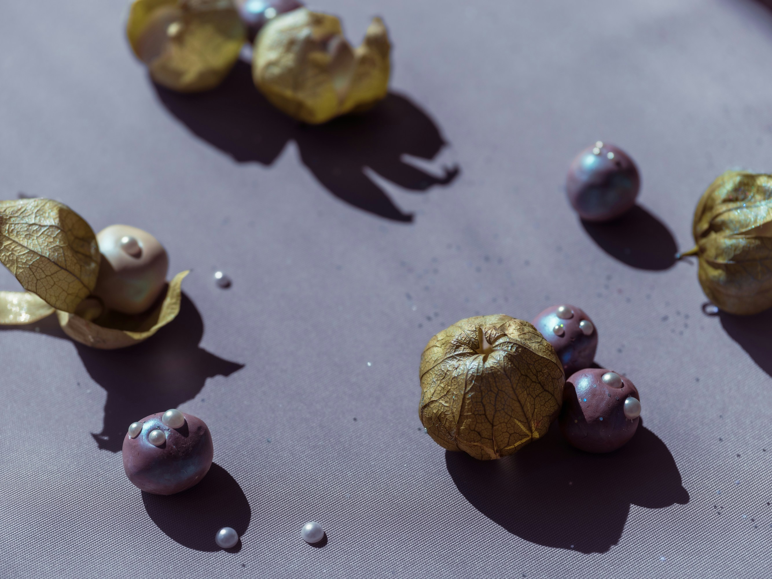Golden physalis husks and small purple spheres with pearls on a grey surface.