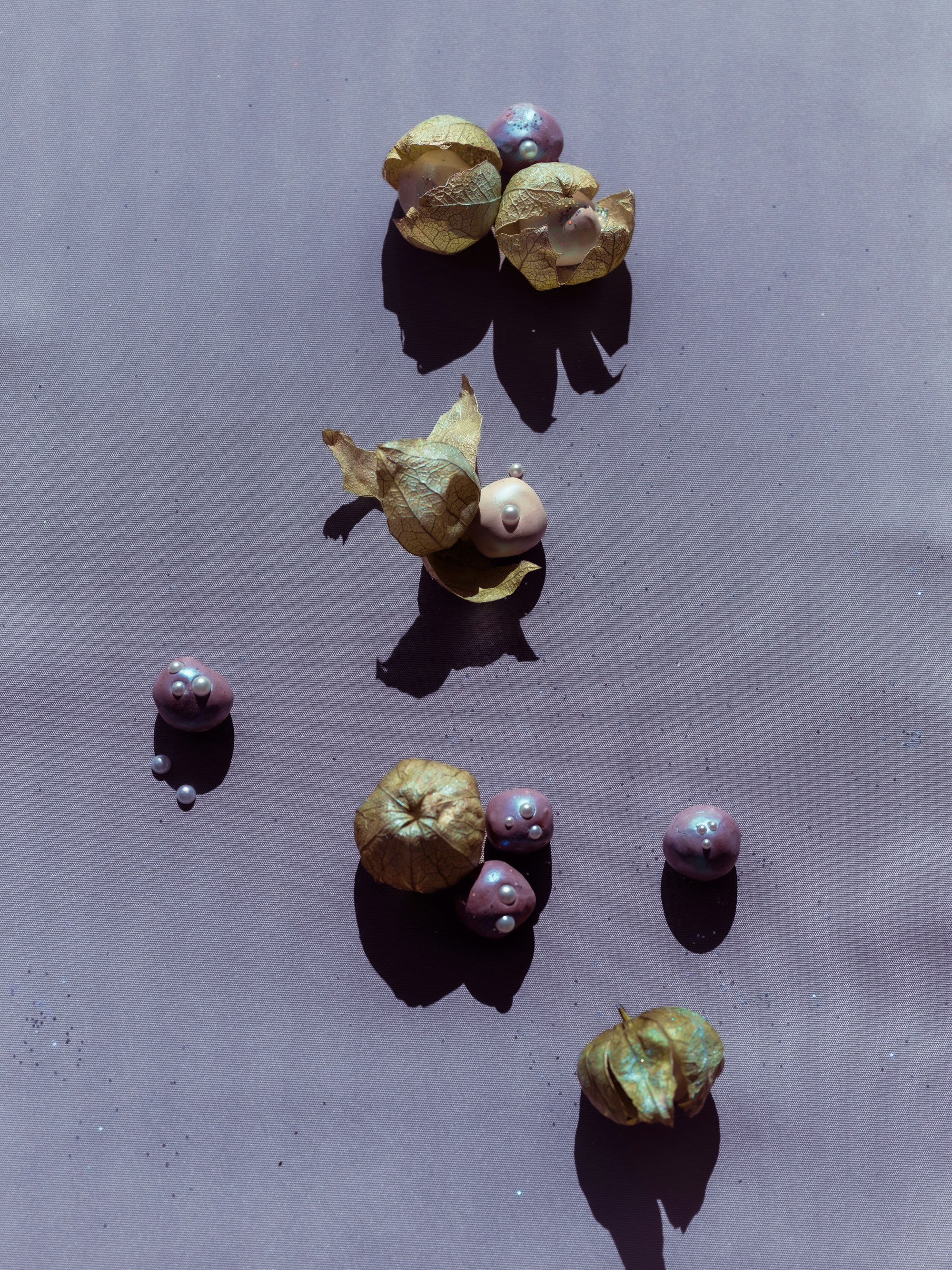 Physalis husks and small purple spheres with pearls on a light purple surface.