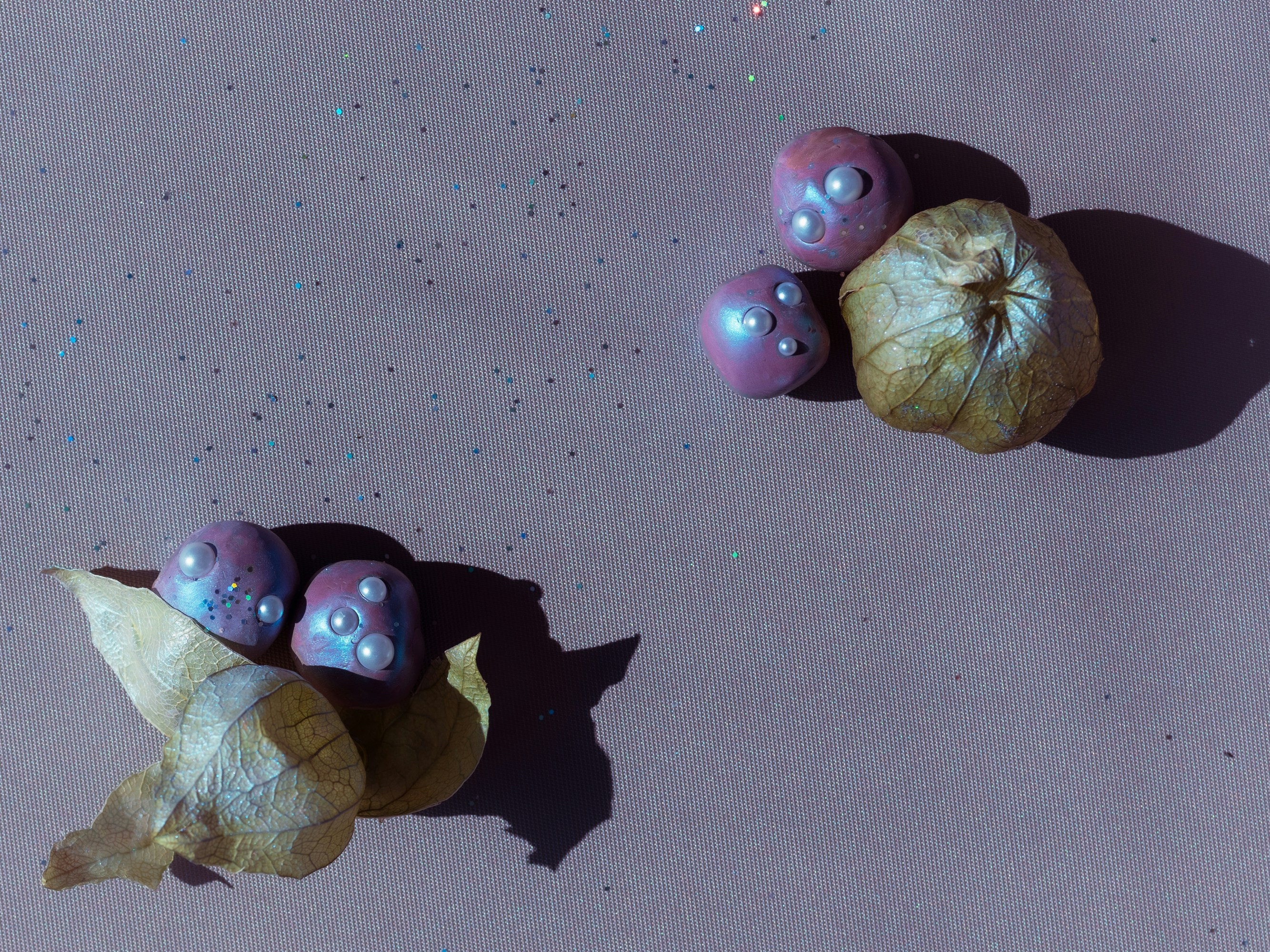 Iridescent purple spheres with pearls and dried physalis husks on a glittery surface.