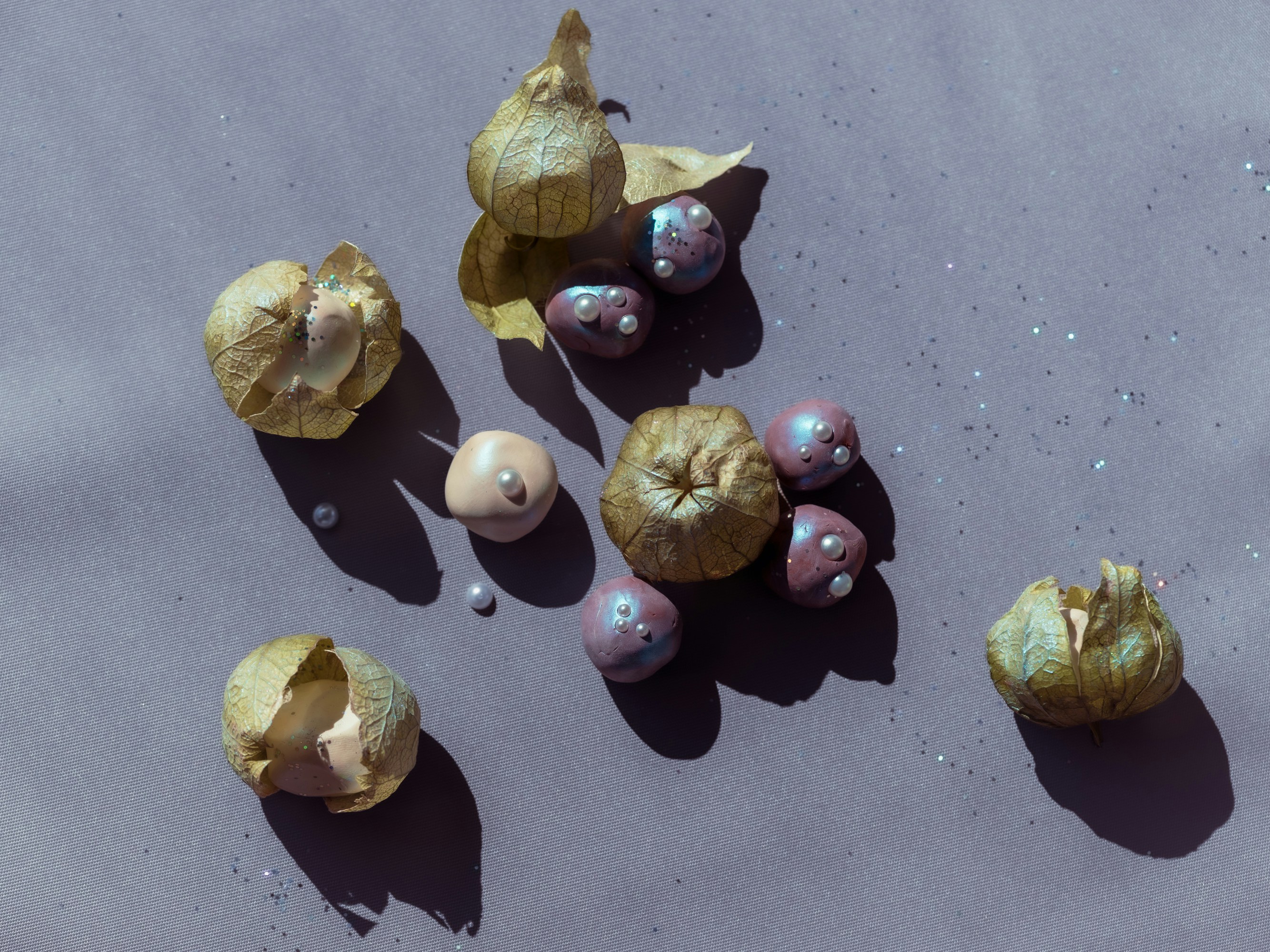Physalis husks and iridescent spheres with small pearls on a light purple surface.