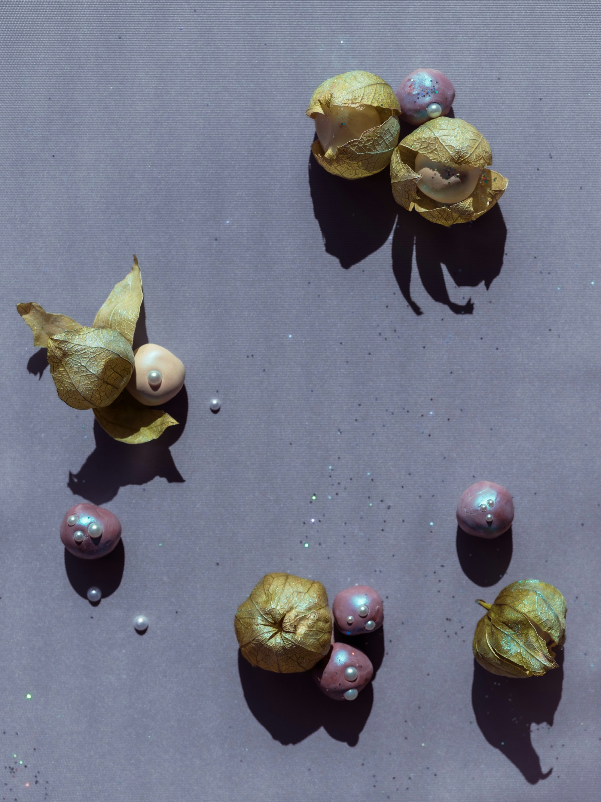 Physalis husks and small iridescent spheres with pearls on a grey surface.