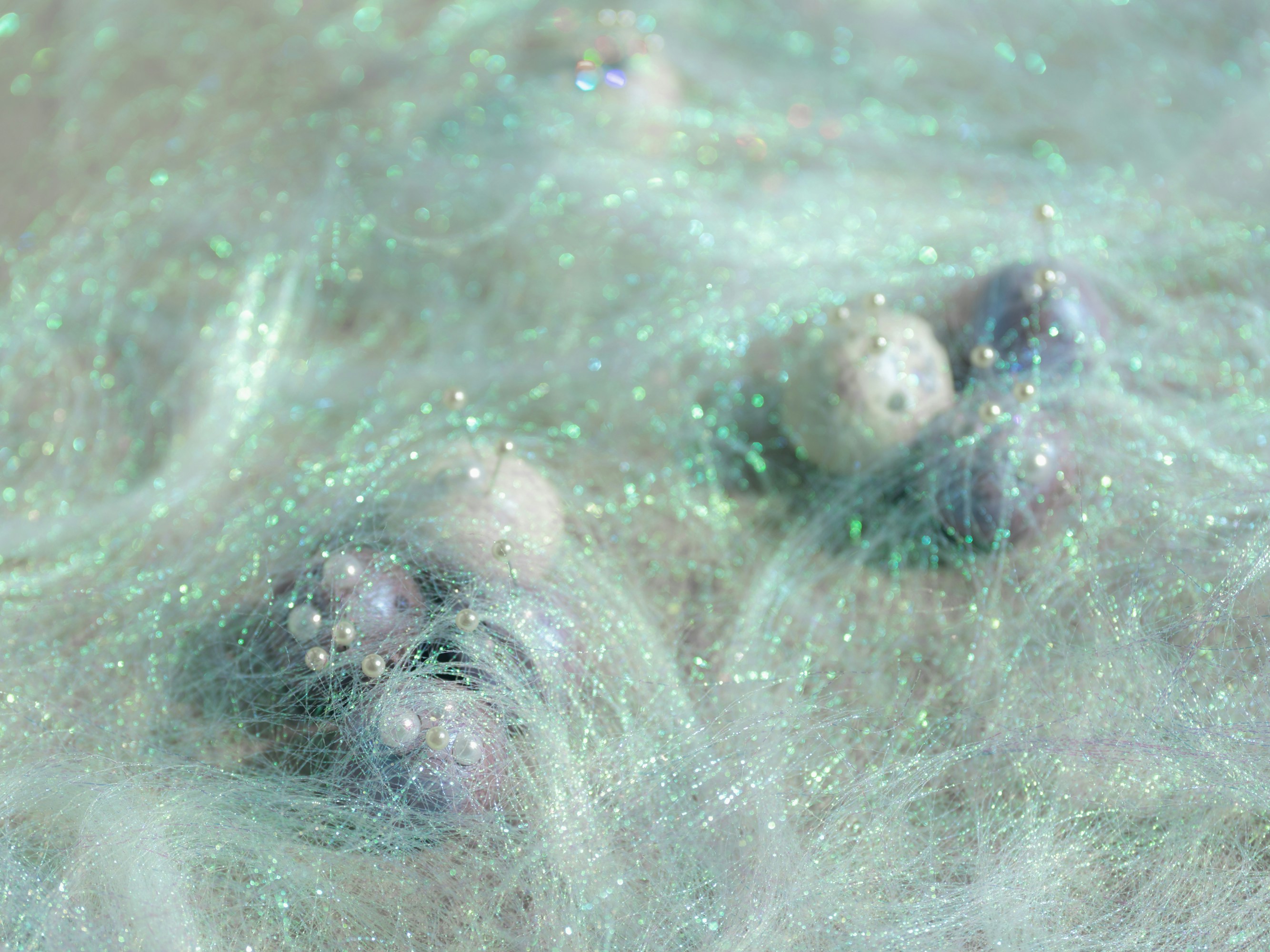 Small spheres with pins nestled in a shimmering, iridescent web of fine fibers.