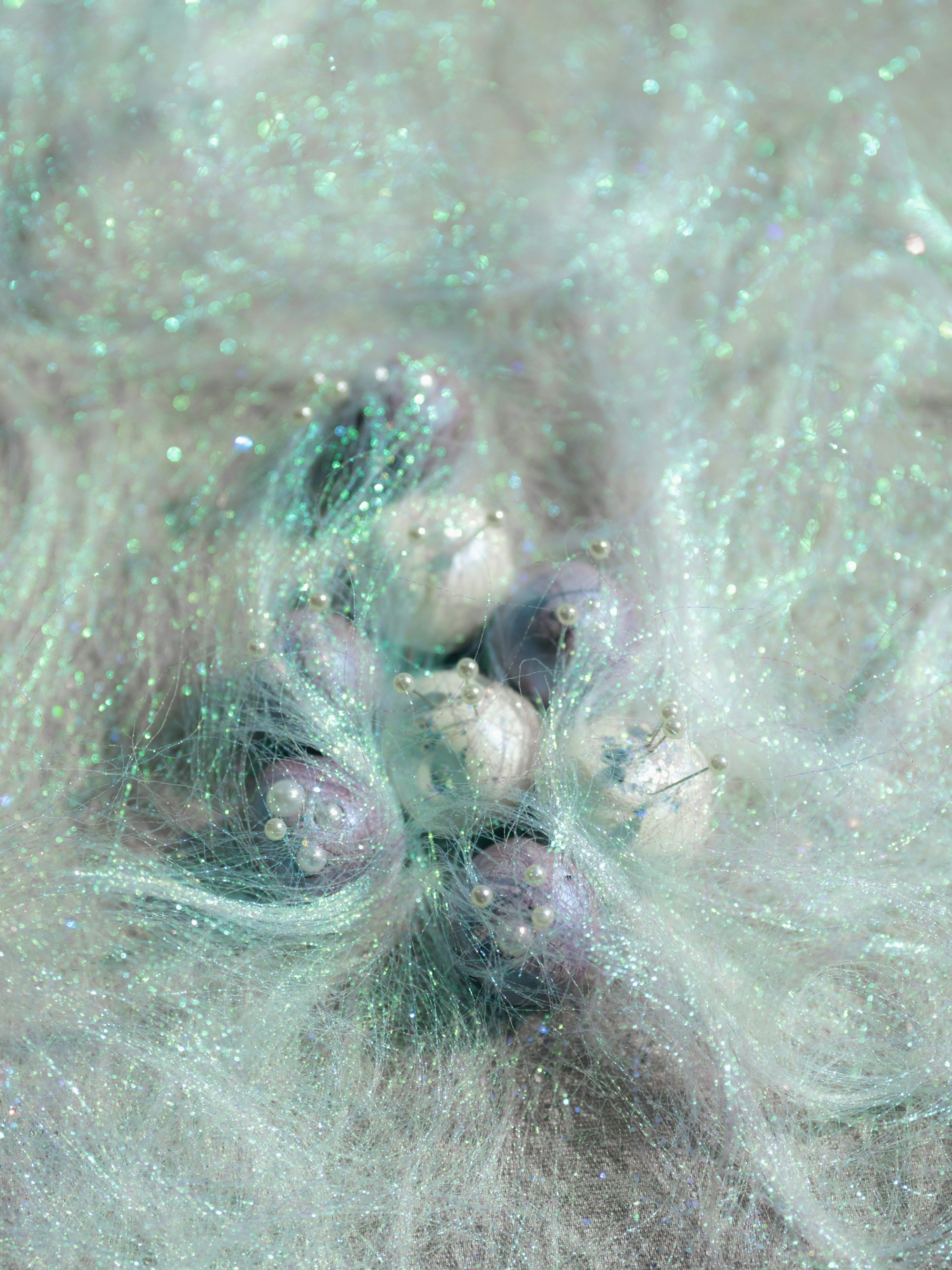 Small spheres with pearl pins nestled in iridescent mint green synthetic hair fibers.