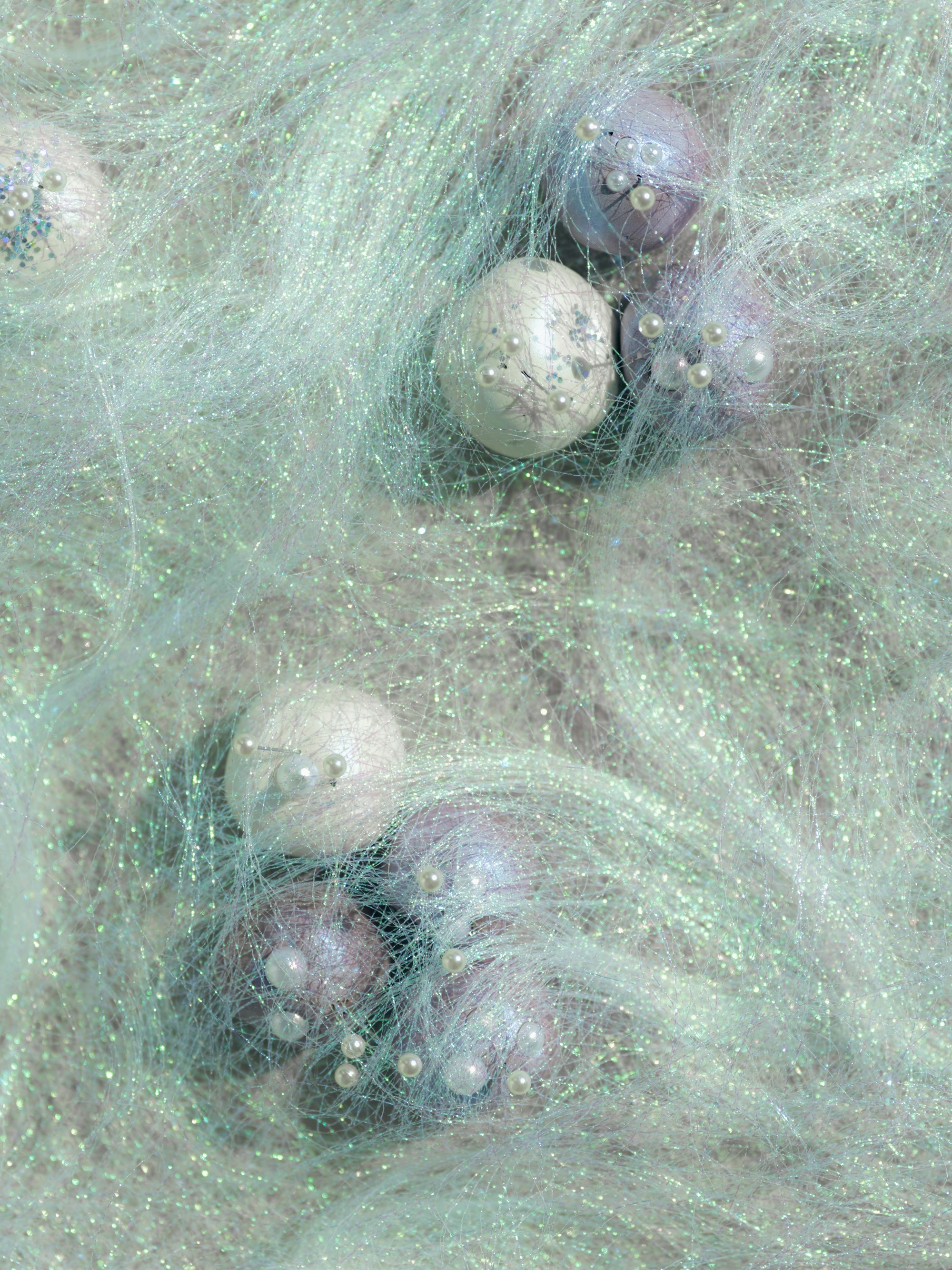 Small decorative spheres with tiny pearls nestled in iridescent mint green fiber.