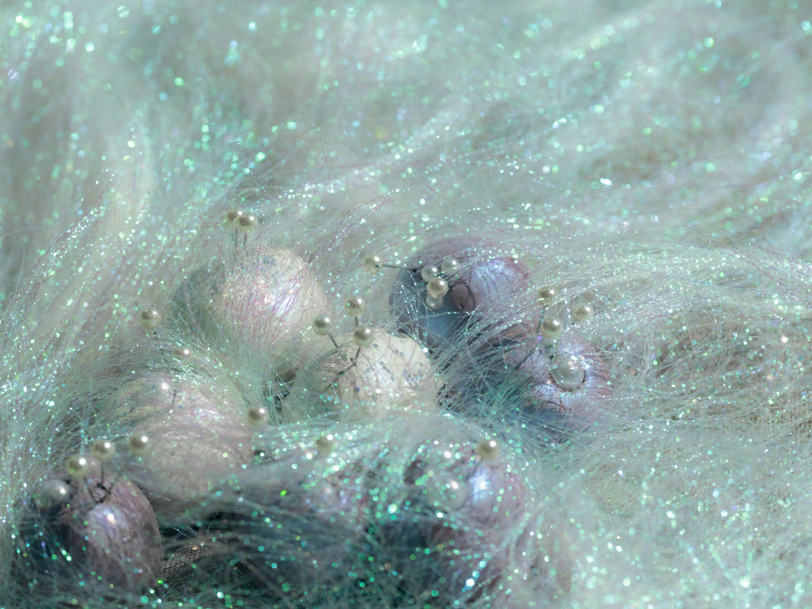 Iridescent spheres with pearl-tipped pins nestled in shimmering, translucent synthetic fibers.