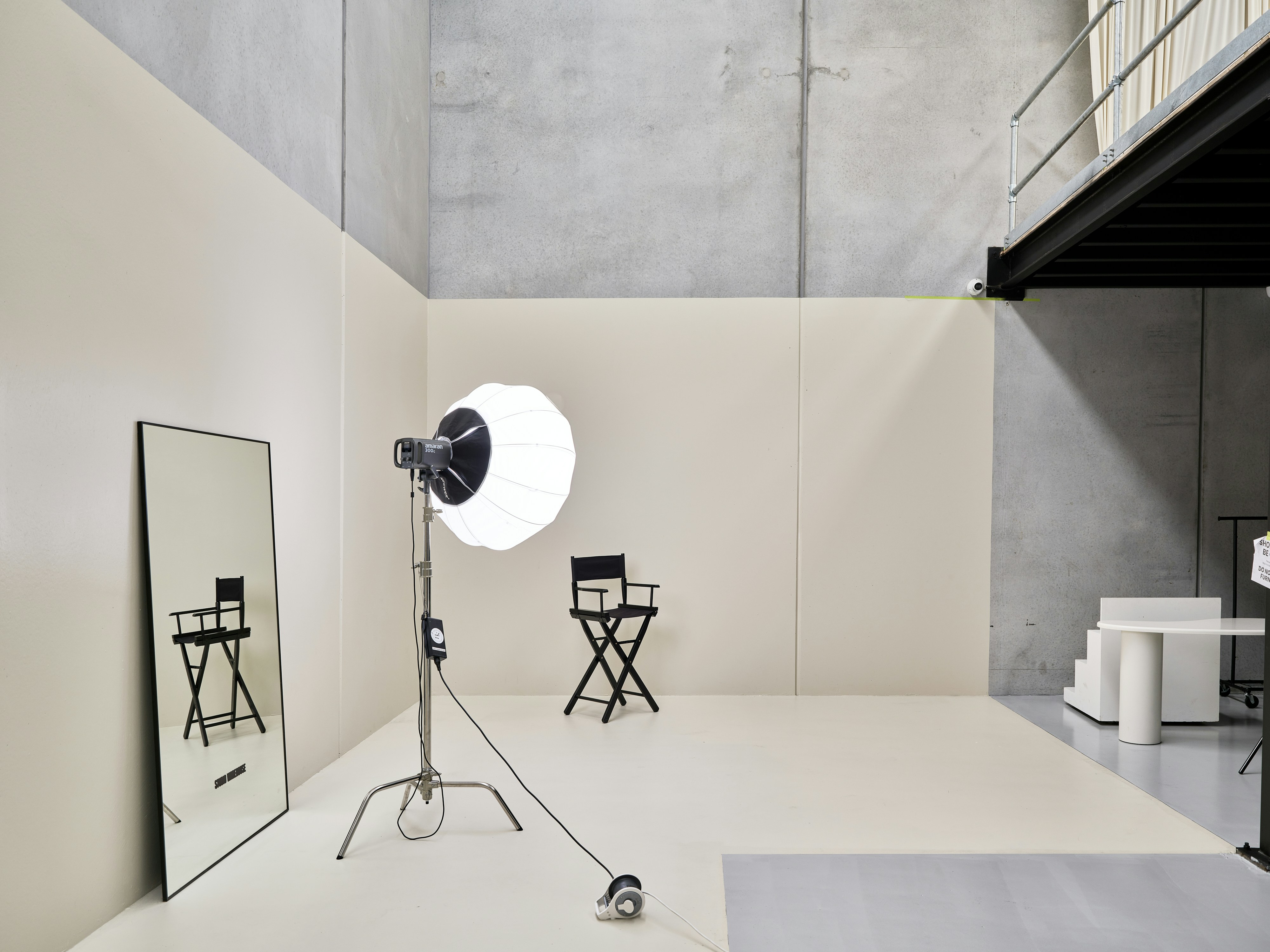A black director chair, a studio light, and a tall mirror in a studio.