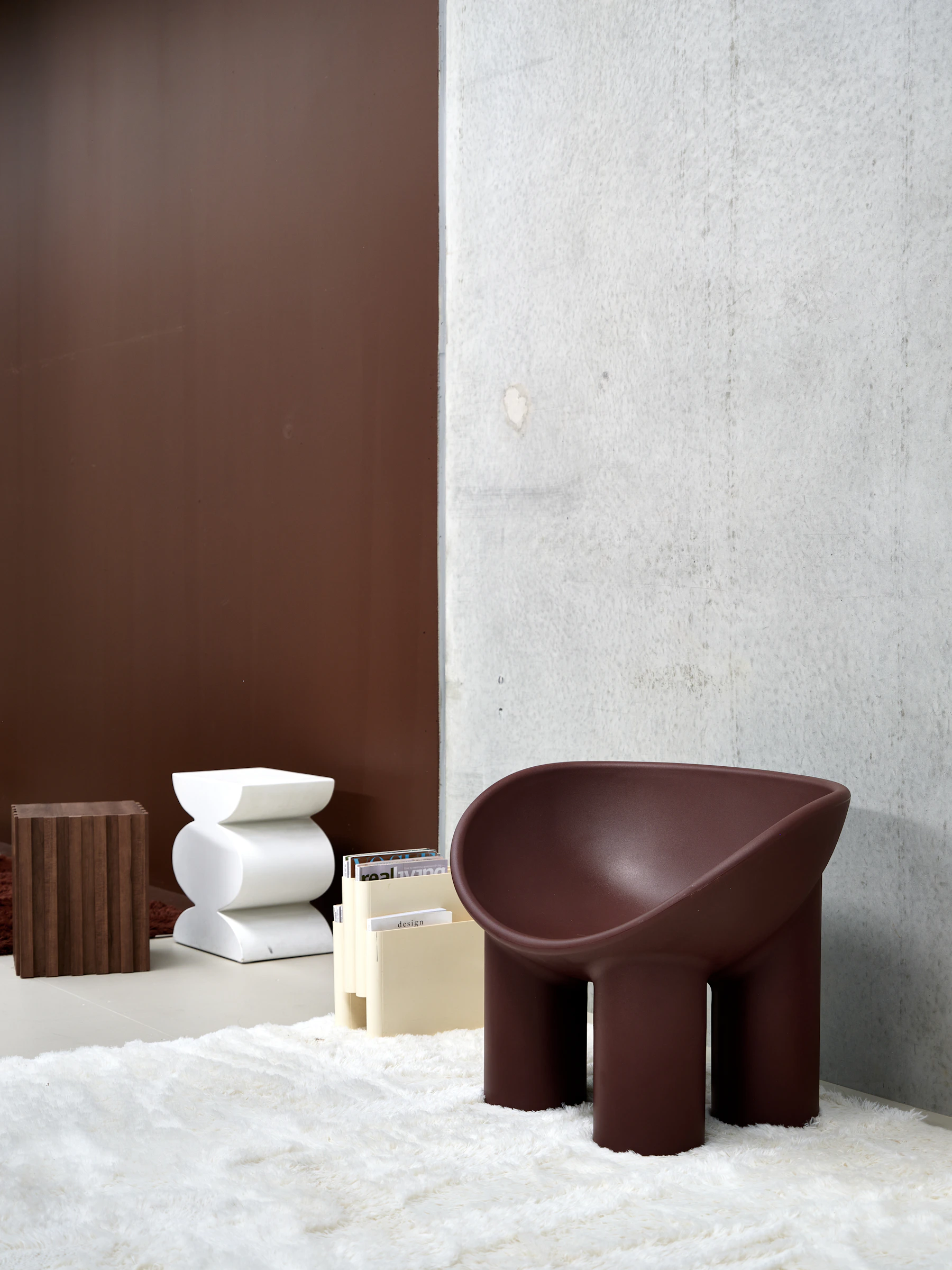 Dark brown sculptural designer chair positioned on a light rug beside a concrete wall