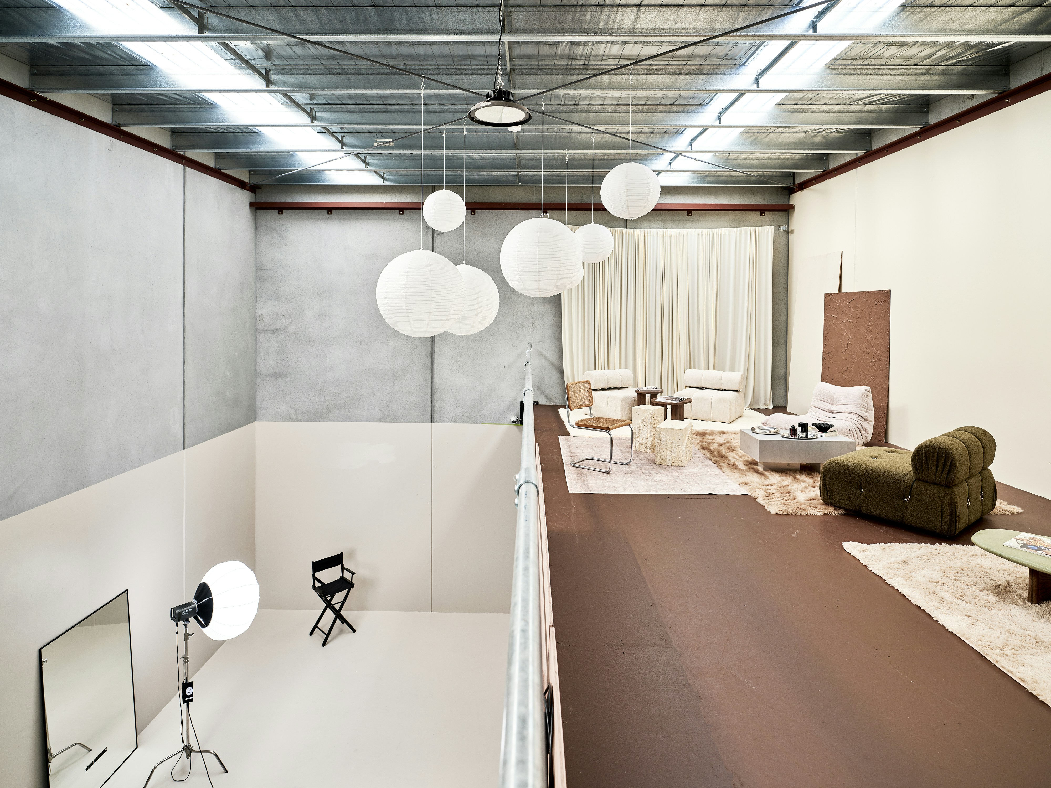 Ruang studio bertingkat dengan lentera kertas, furnitur lounge, dan kursi sutradara