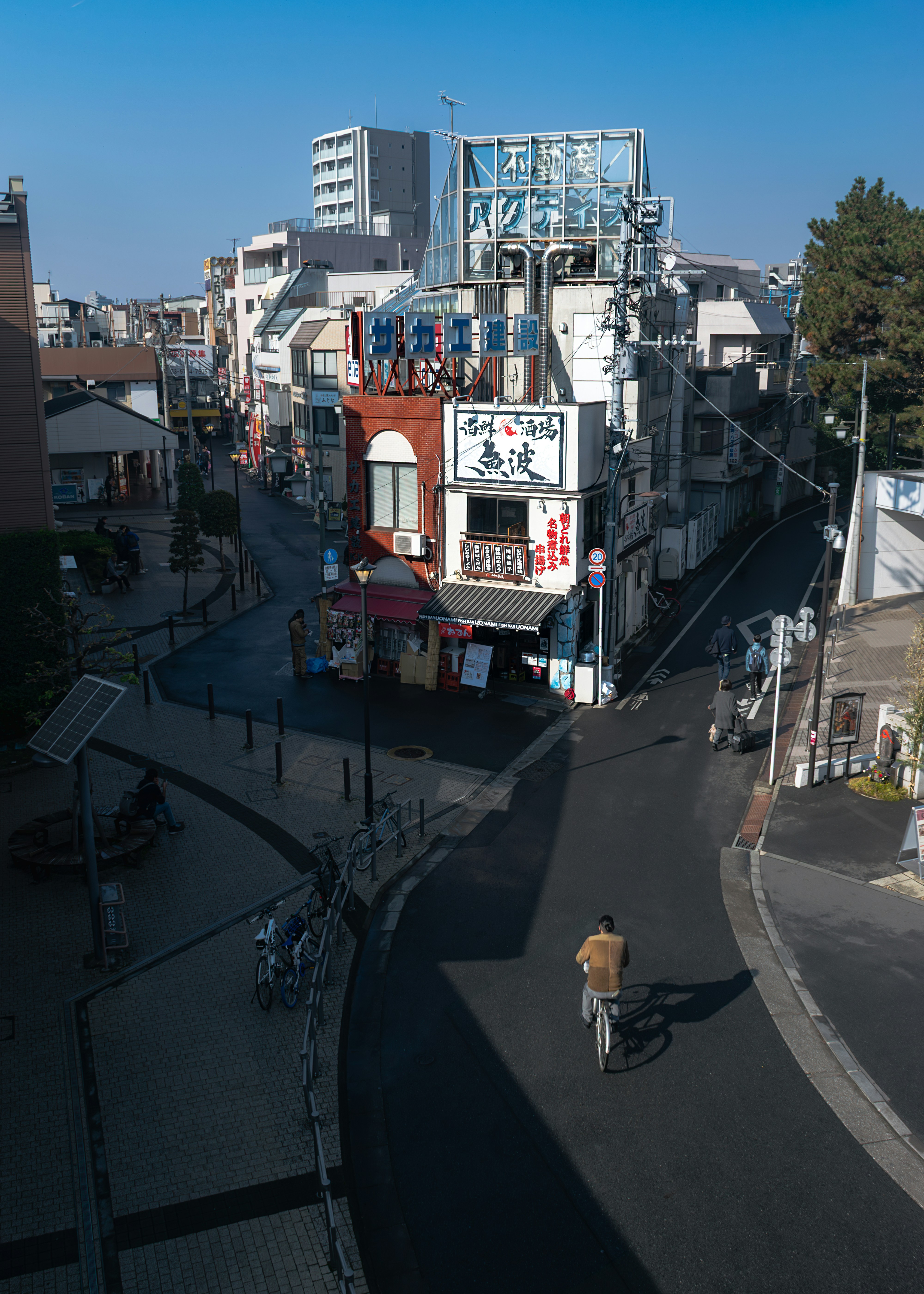 A person cycling on a street near a corner building with Japanese signage.