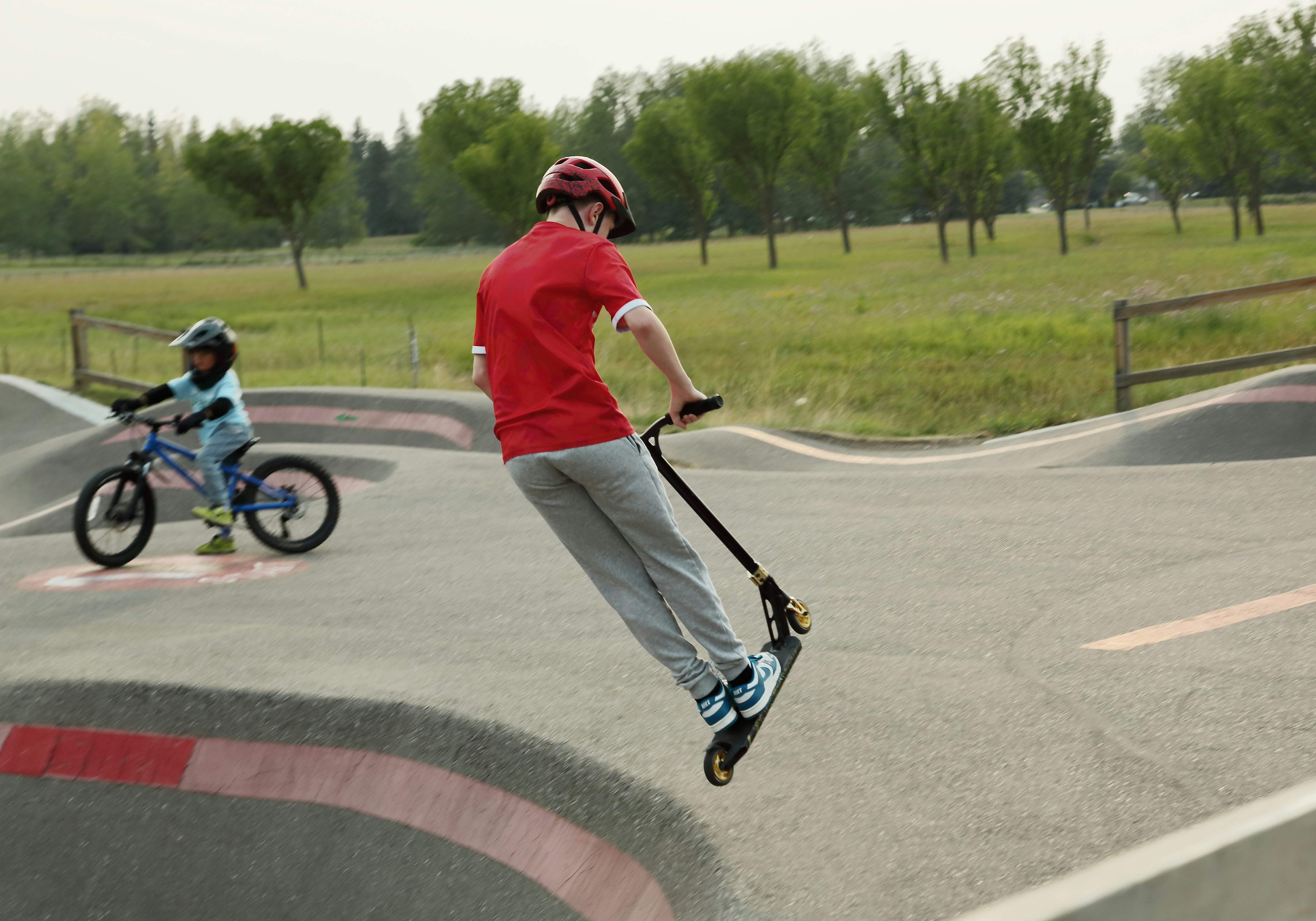 A person in a red shirt riding a scooter on a paved pump track.