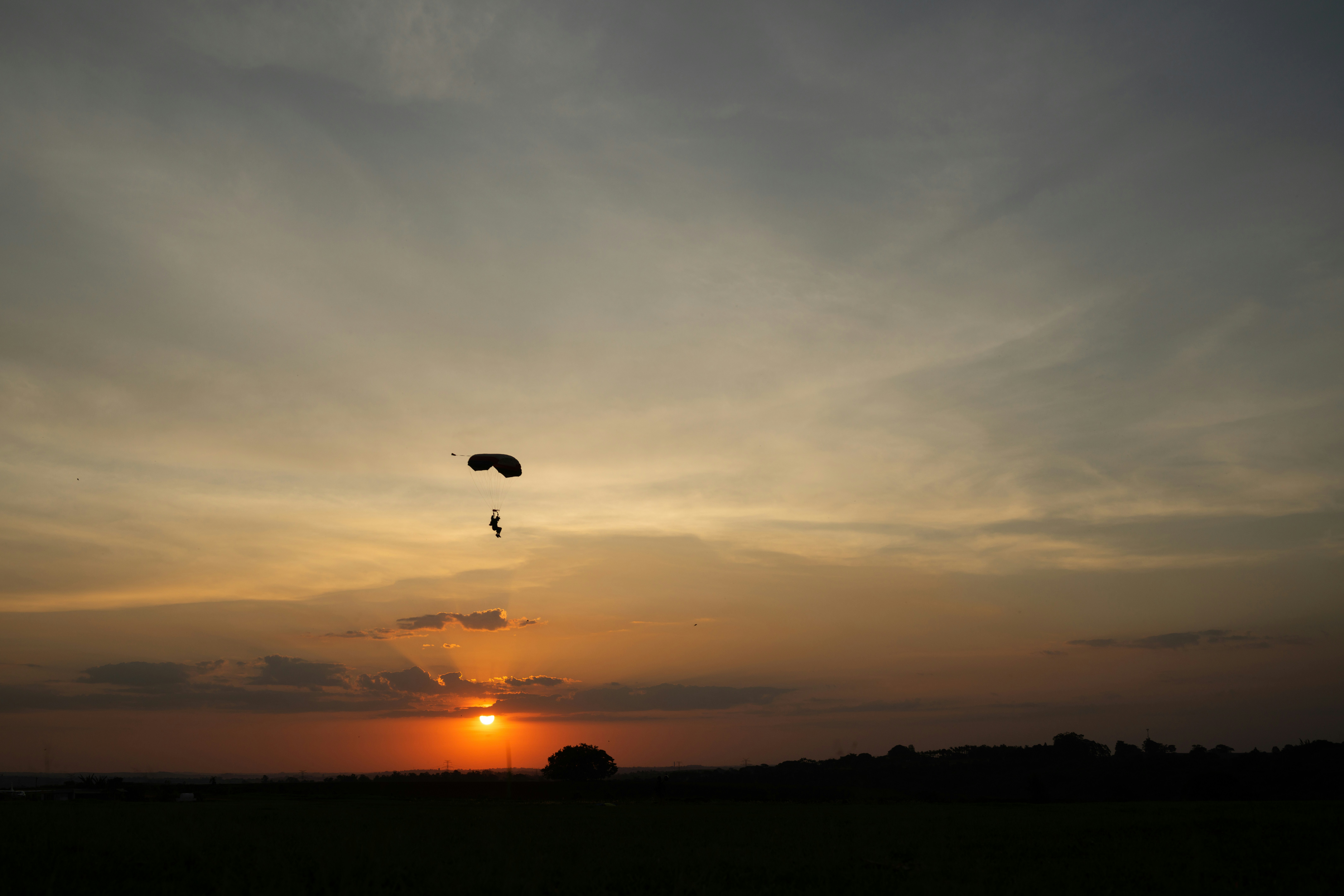 Sebuah paralayang dalam siluet melawan langit oranye hangat dengan matahari rendah