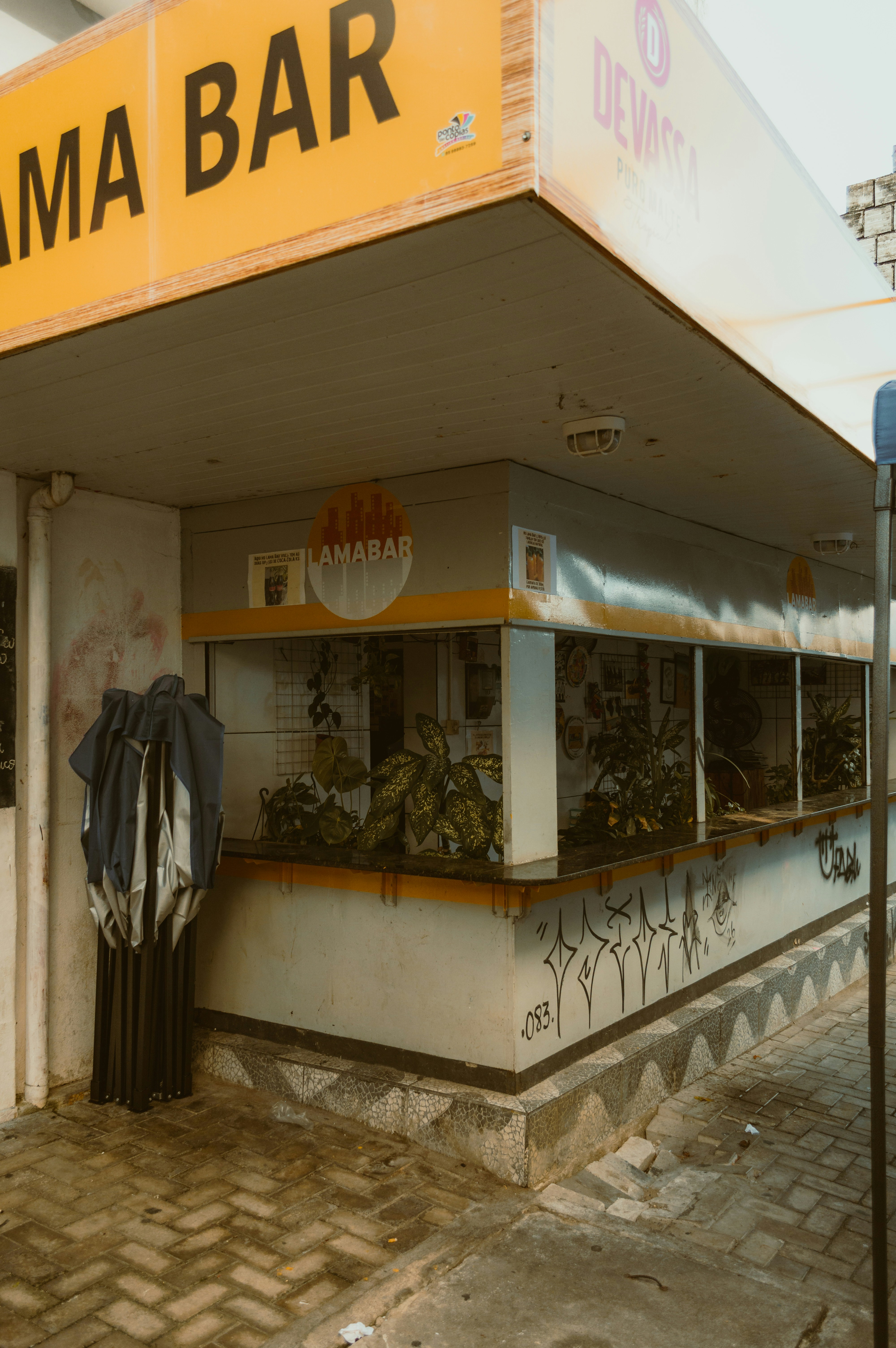 Sebuah bar di tingkat jalan dengan papan kuning bertuliskan "LAMA BAR" dan dinding yang penuh grafiti.