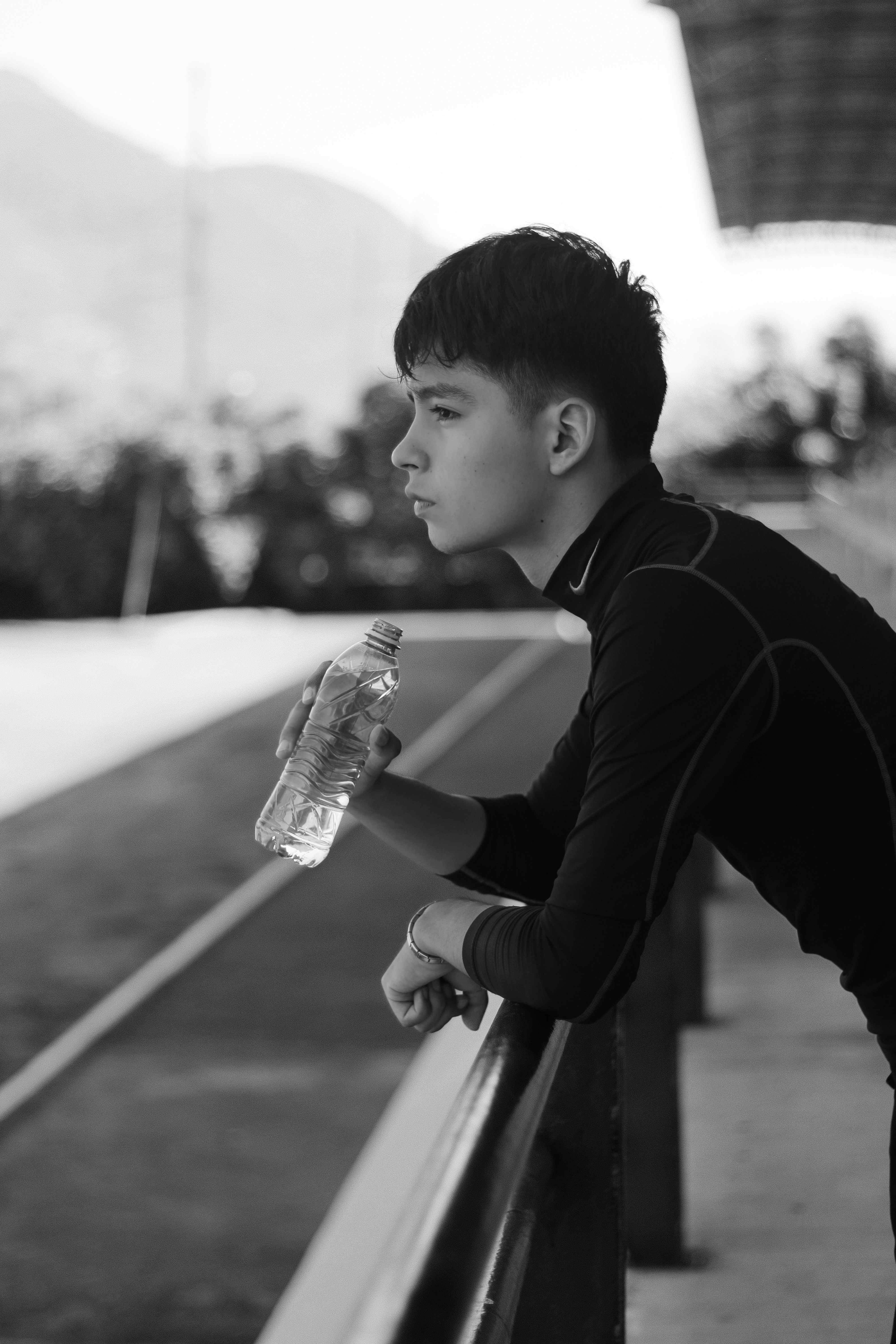 A young man in a black athletic shirt holding a water bottle on a track