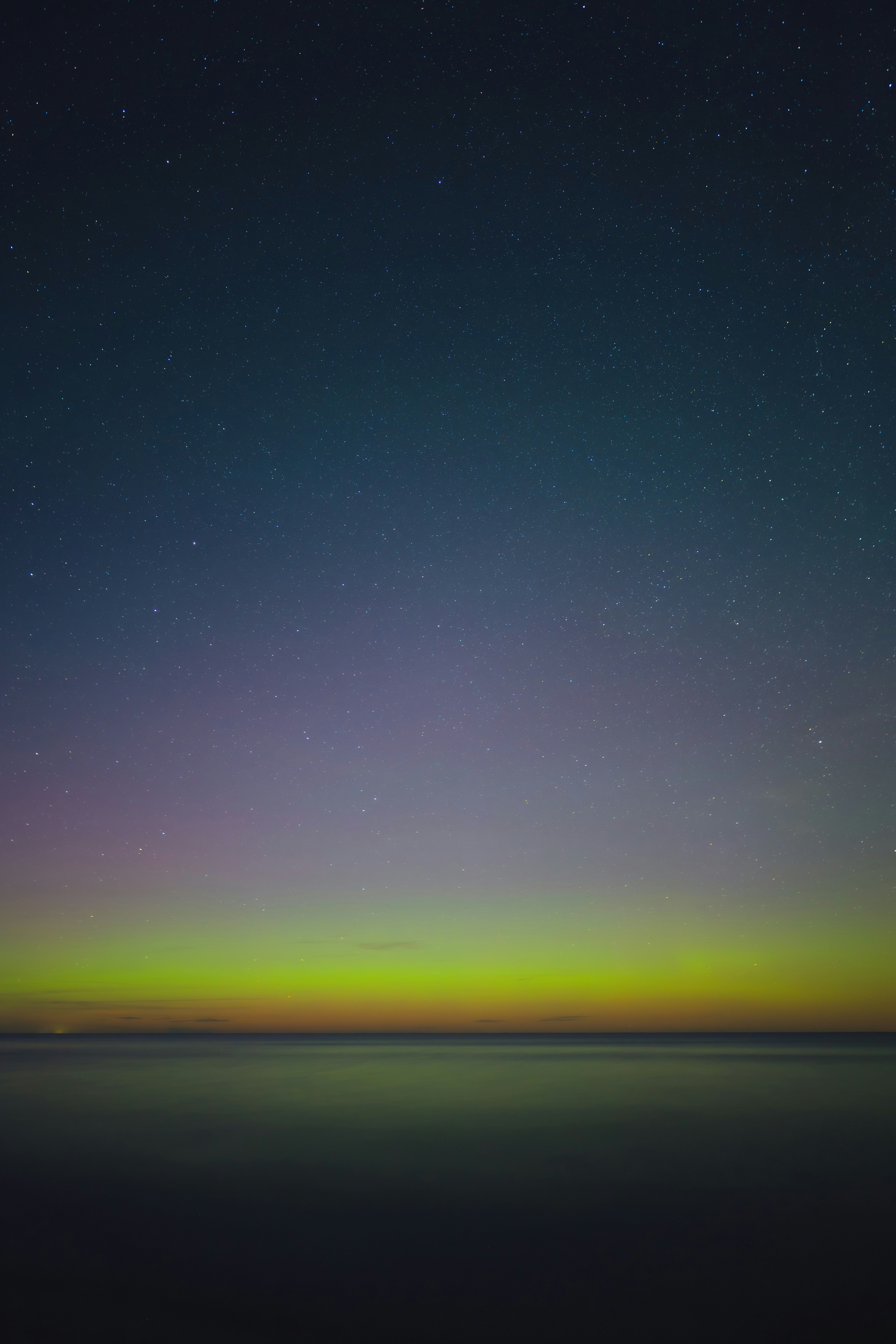 Aurora boreal verde brilhando sobre um oceano escuro e calmo sob um céu estrelado