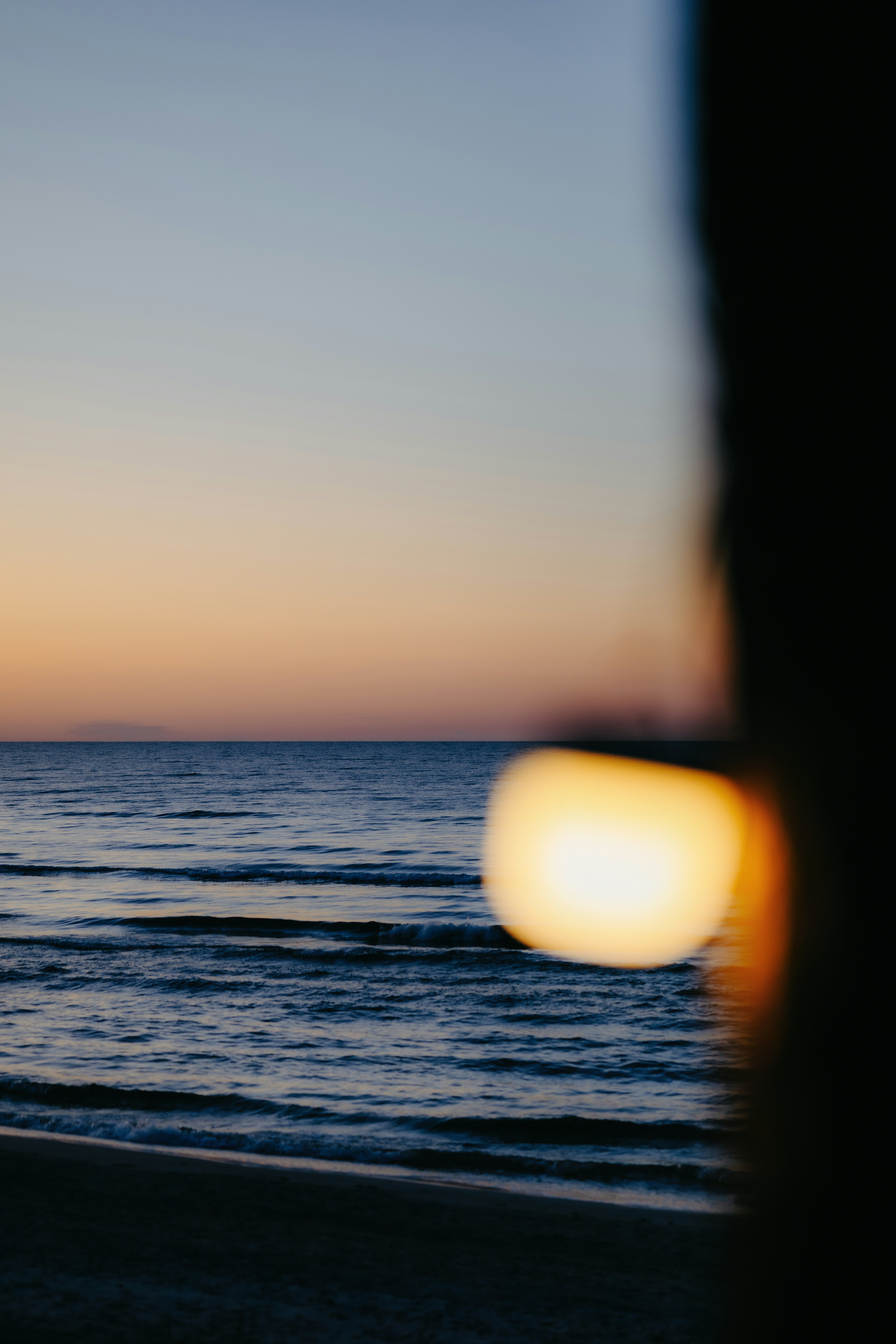 A blurred glowing light bulb against a calm sea under a gradient sky.