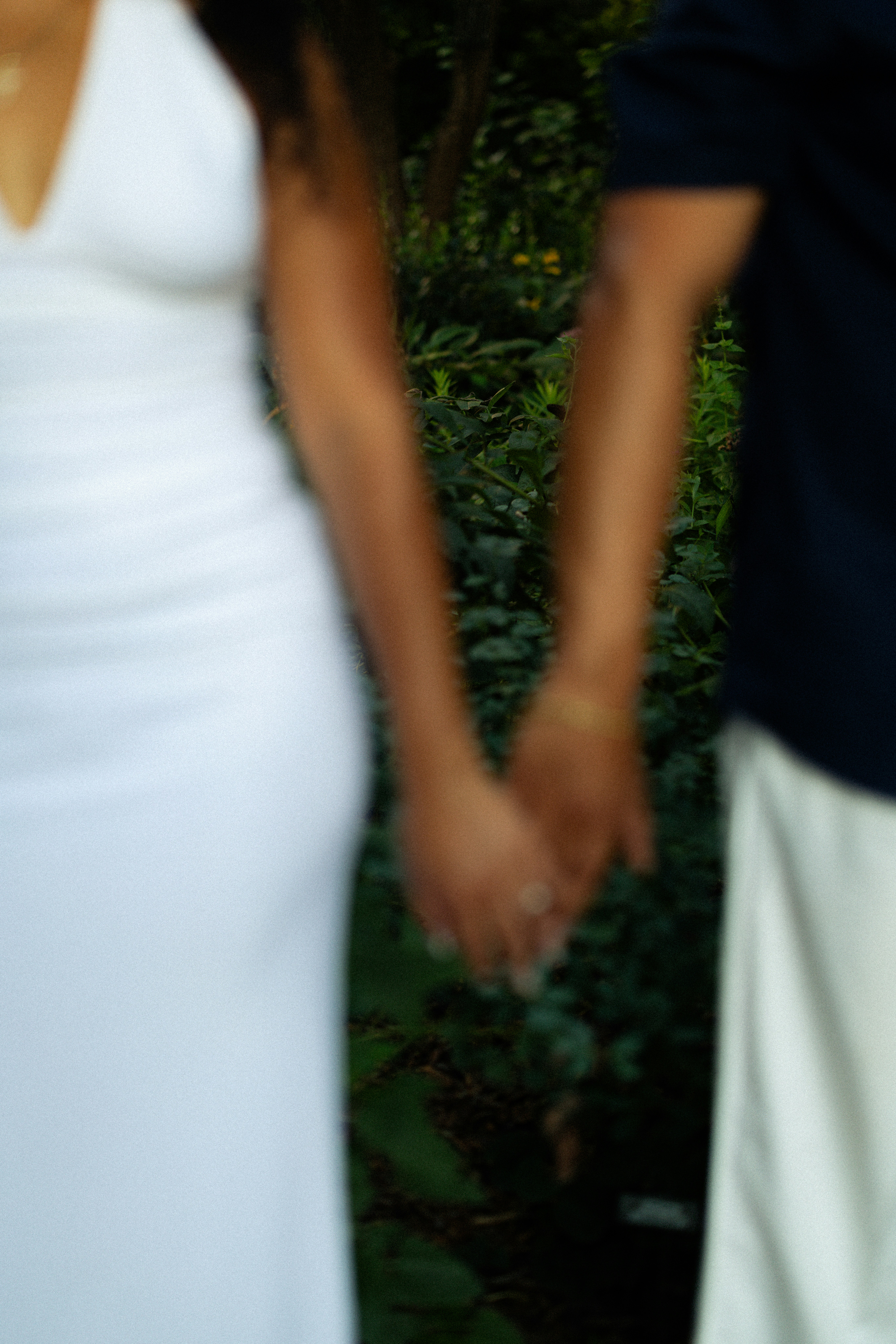 Two people holding hands in a garden, one in a white dress