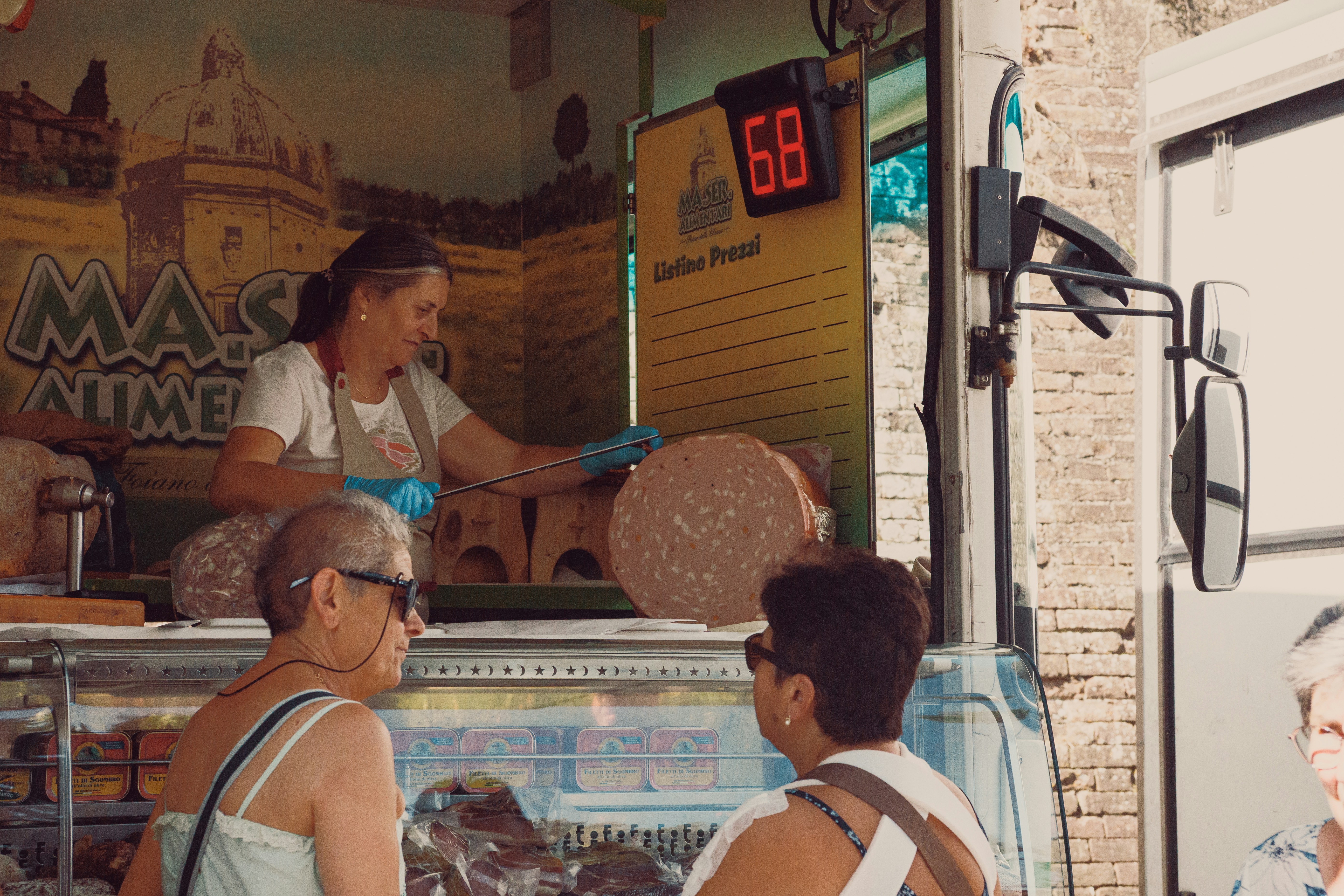 A woman in an apron slicing mortadella at a deli counter for customers
