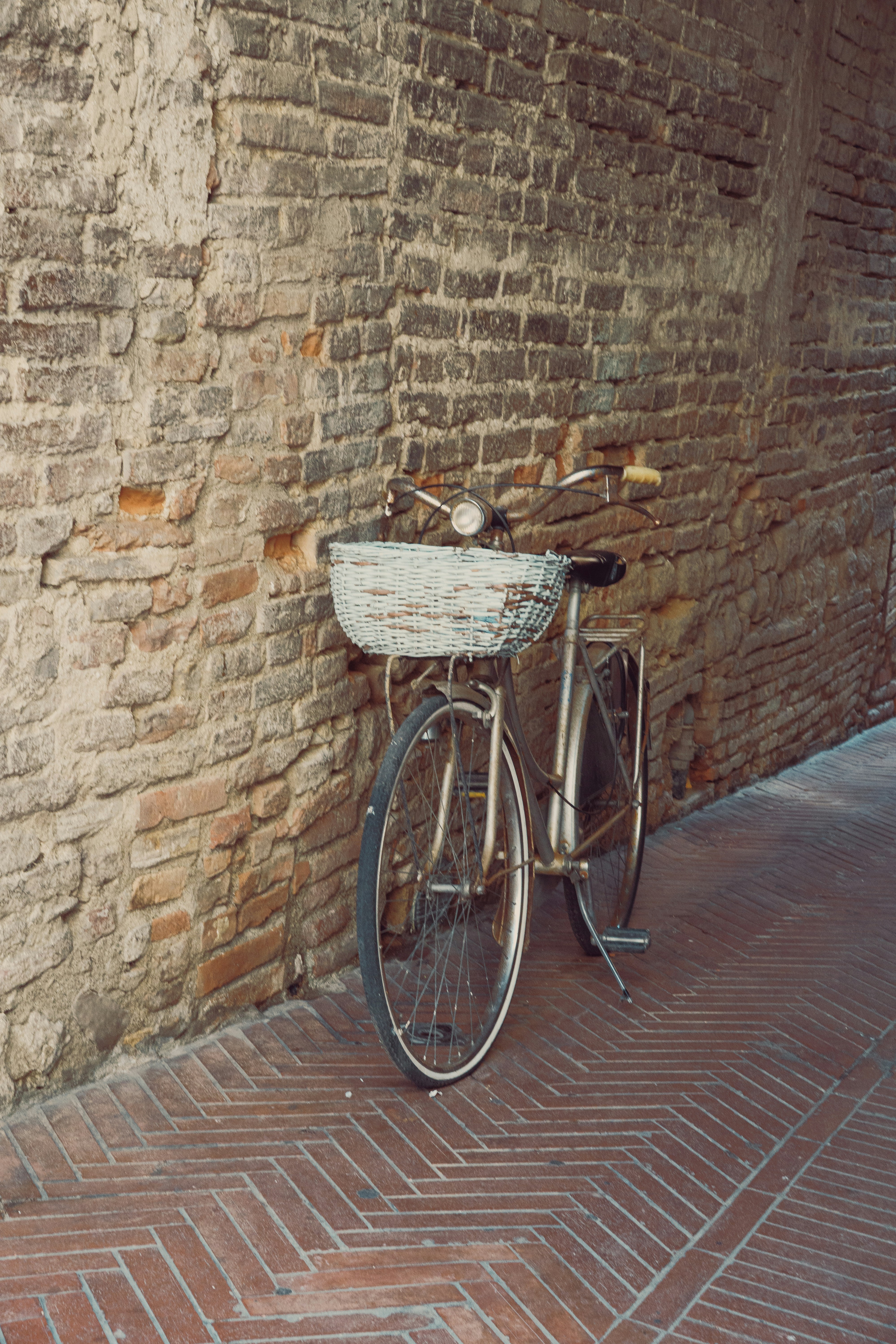 A vintage bicycle with a wicker basket against a weathered brick wall