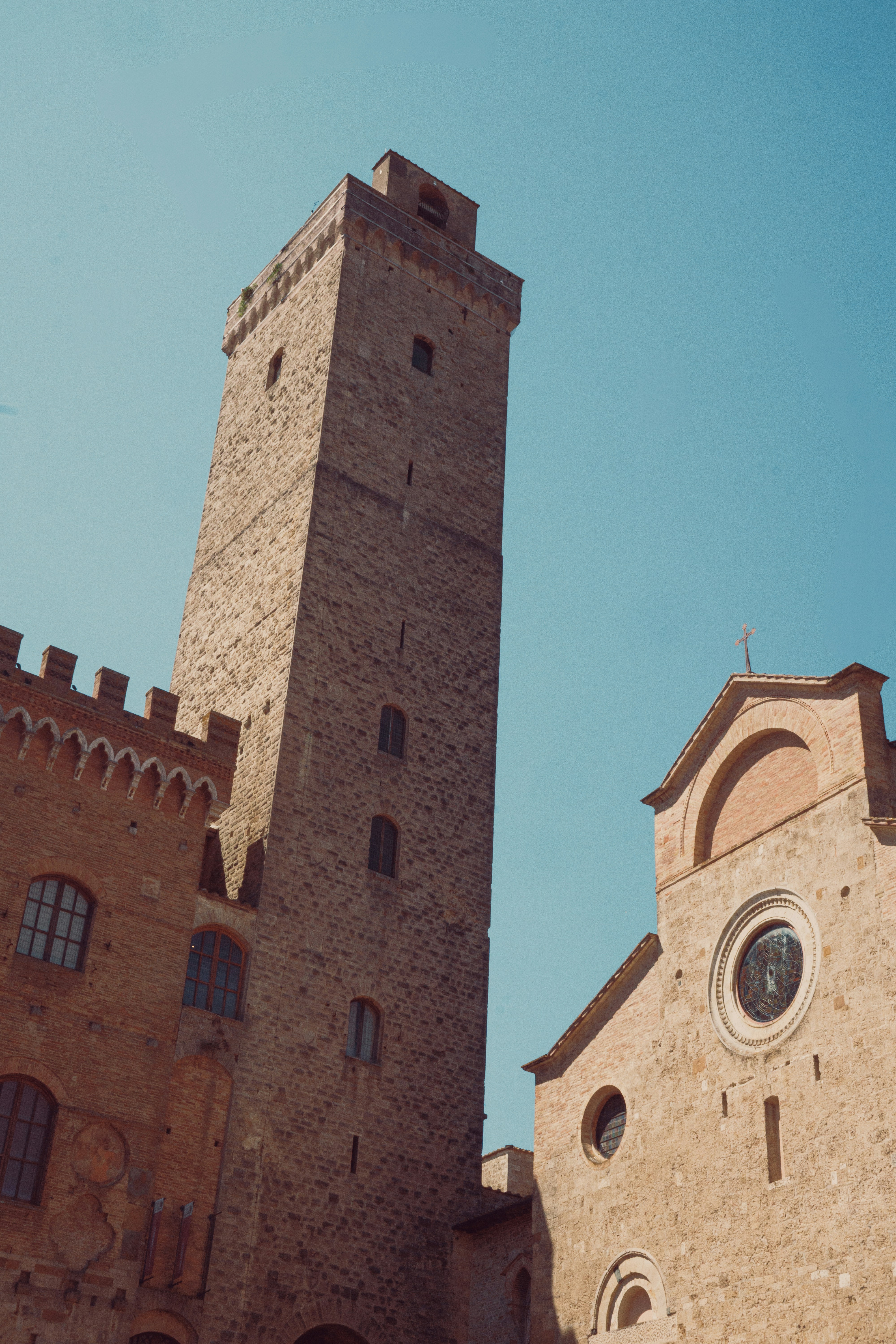 A tall stone tower beside a medieval brick church under a clear blue sky