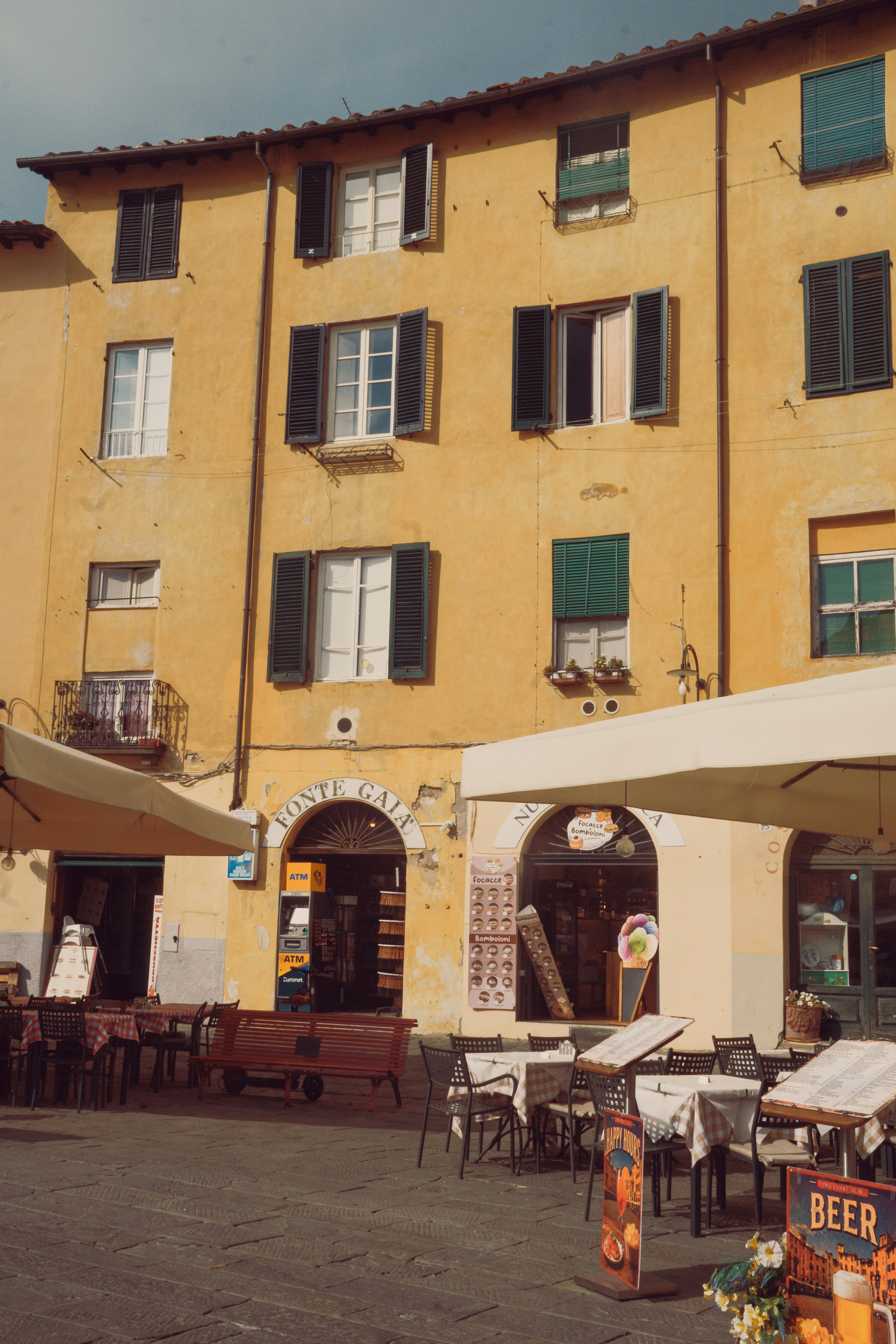 Outdoor cafe tables with umbrellas in front of a yellow building in Lucca