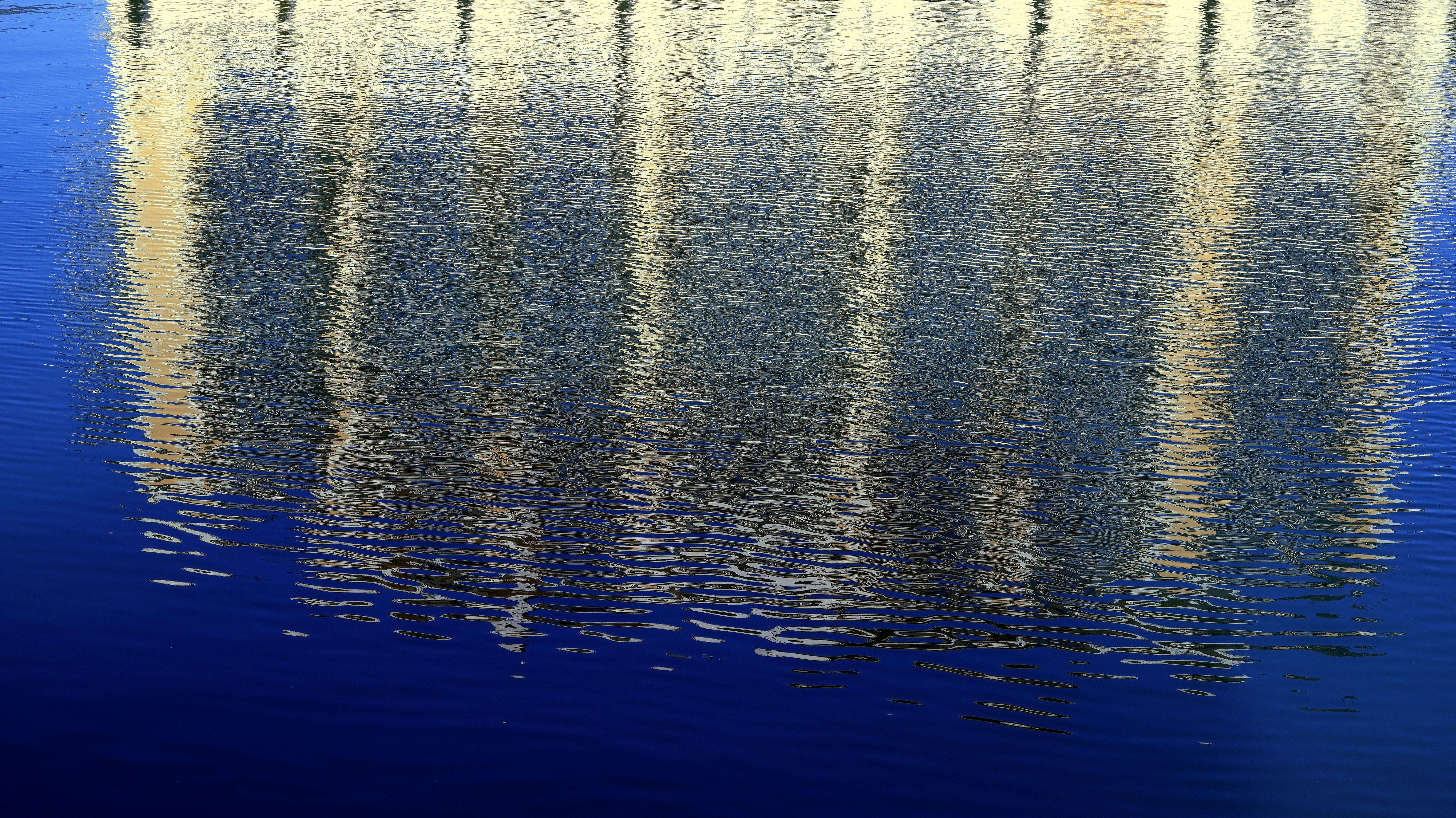 The reflection of a building with white columns on rippling dark blue water