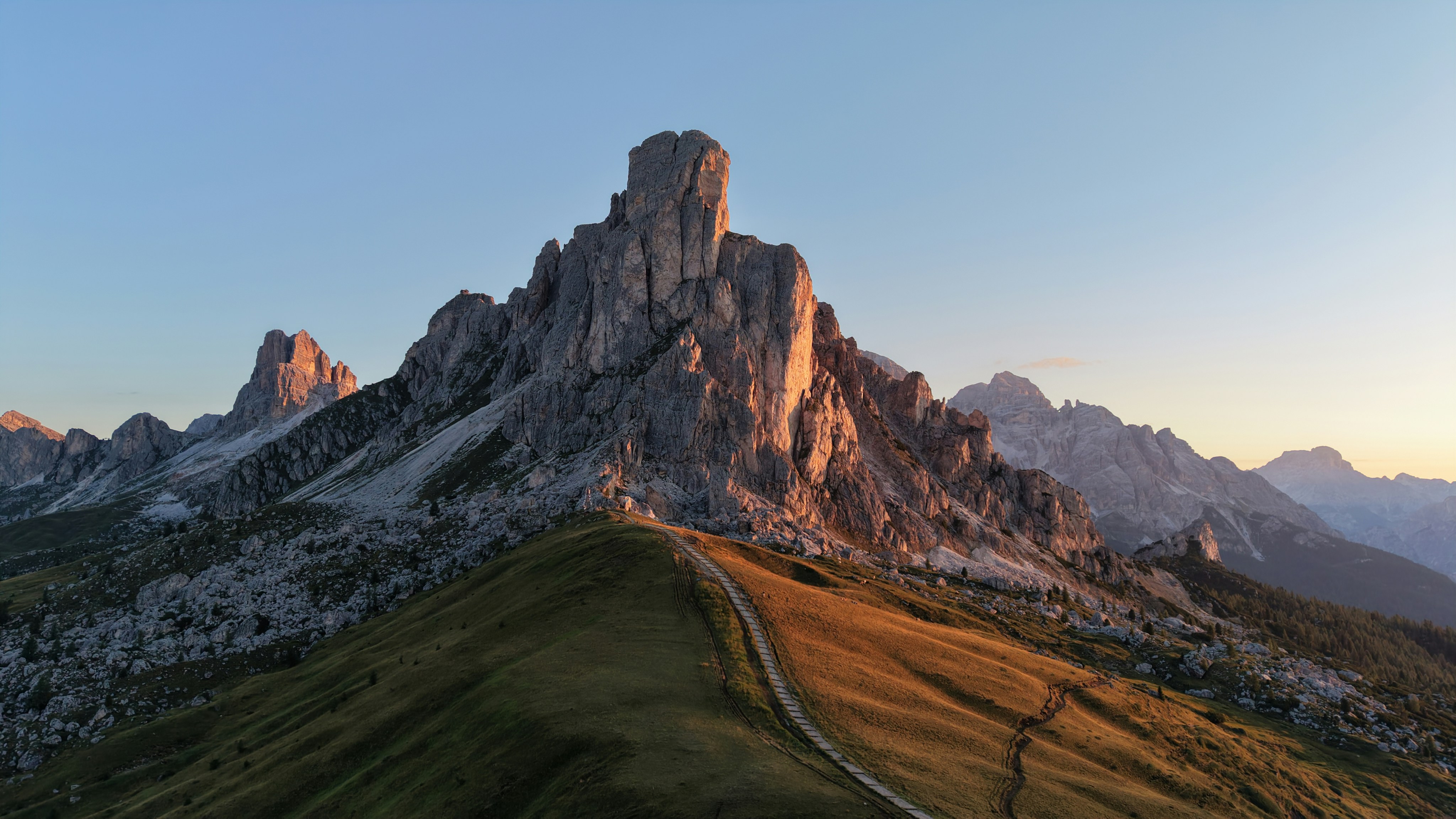 A narrow hiking trail winding up a grassy slope toward jagged rocky peaks.
