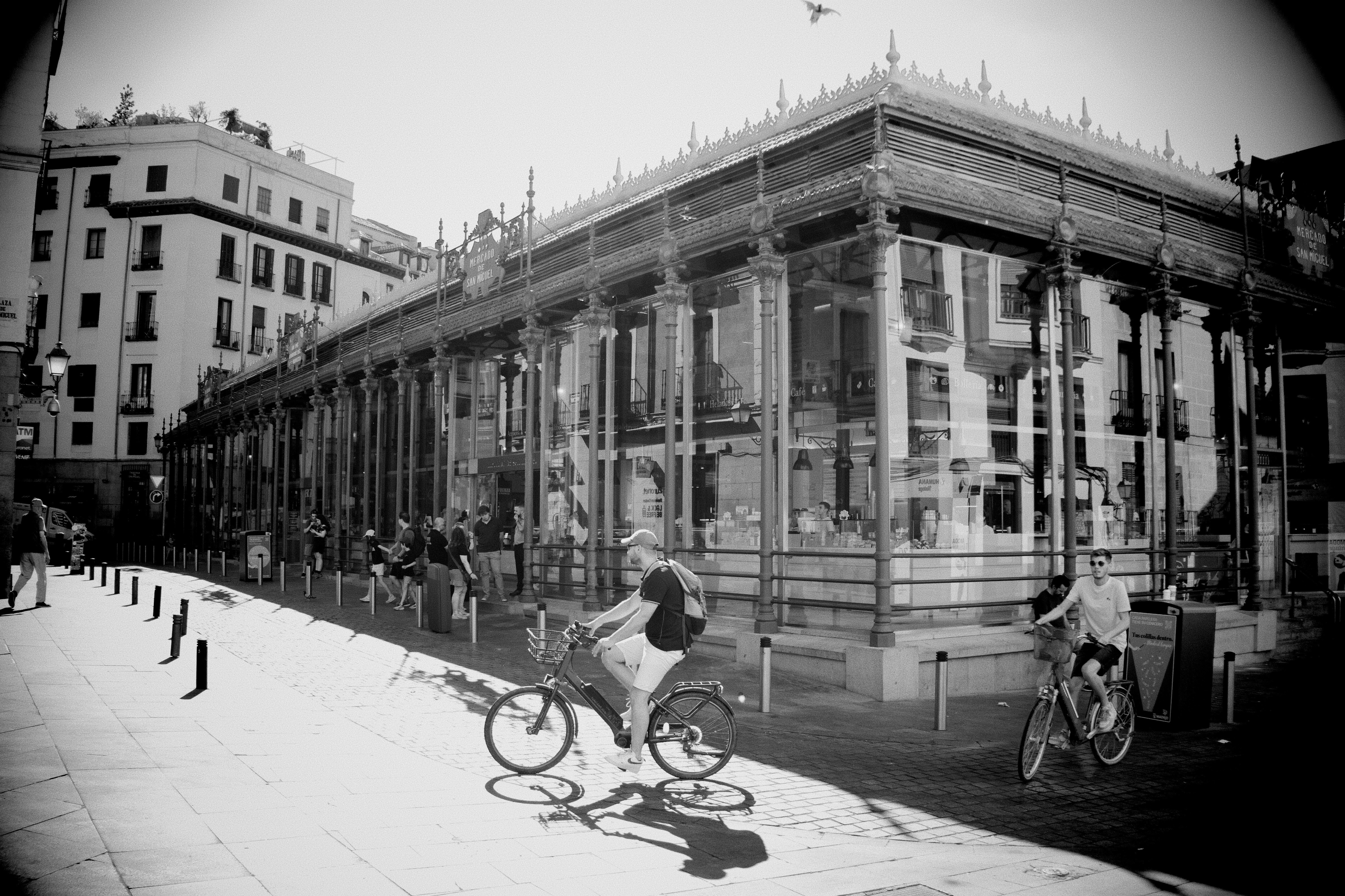 Two people cycling past the Mercado de San Miguel in Madrid