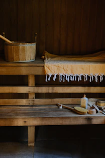 A wooden sauna bench with a bucket, yellow towel, and bath accessories