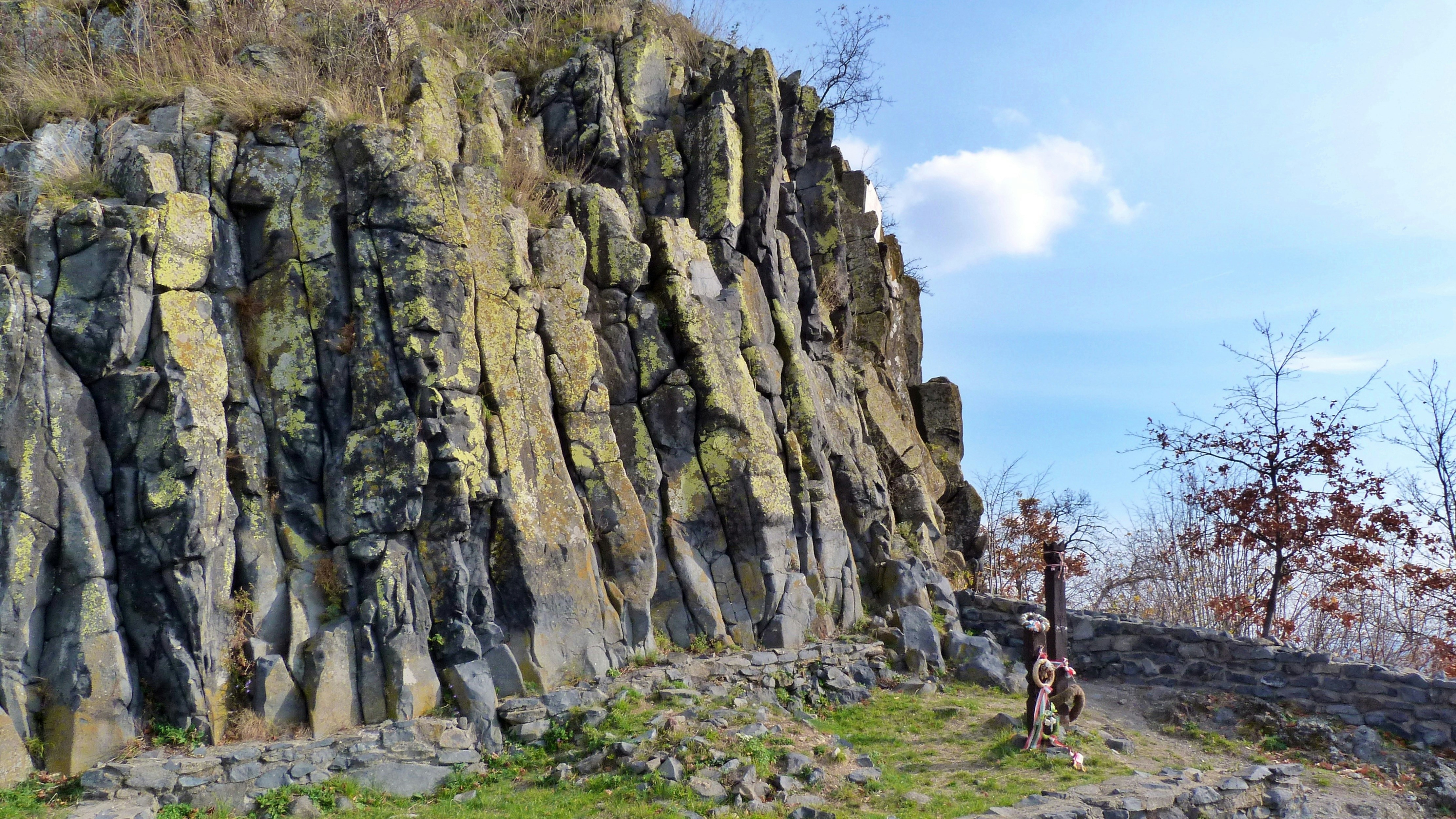 A tall basalt rock formation with vertical columns covered in yellow lichen